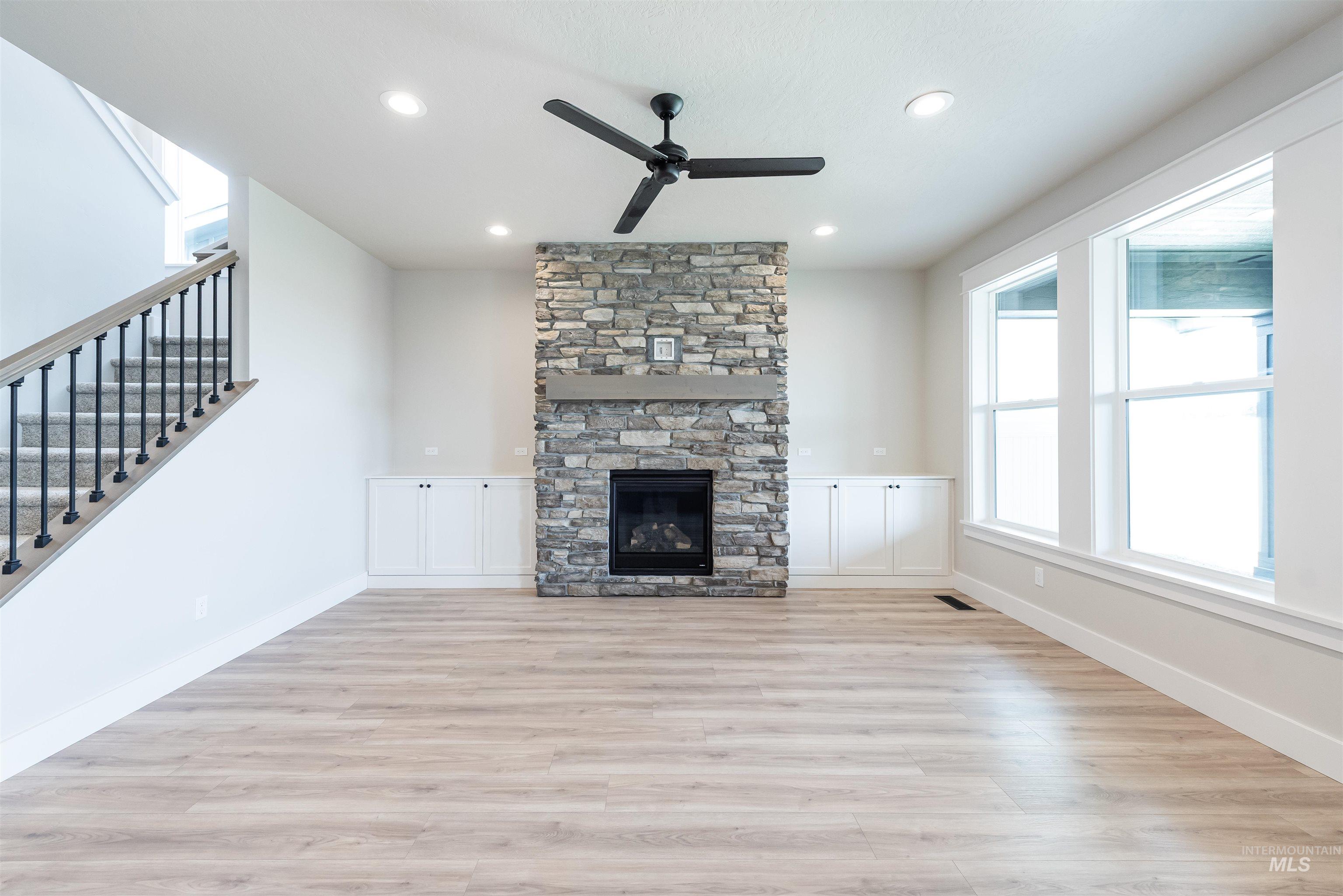 Unfurnished living room with light wood finished floors, stairs, ceiling fan, a fireplace, and recessed lighting