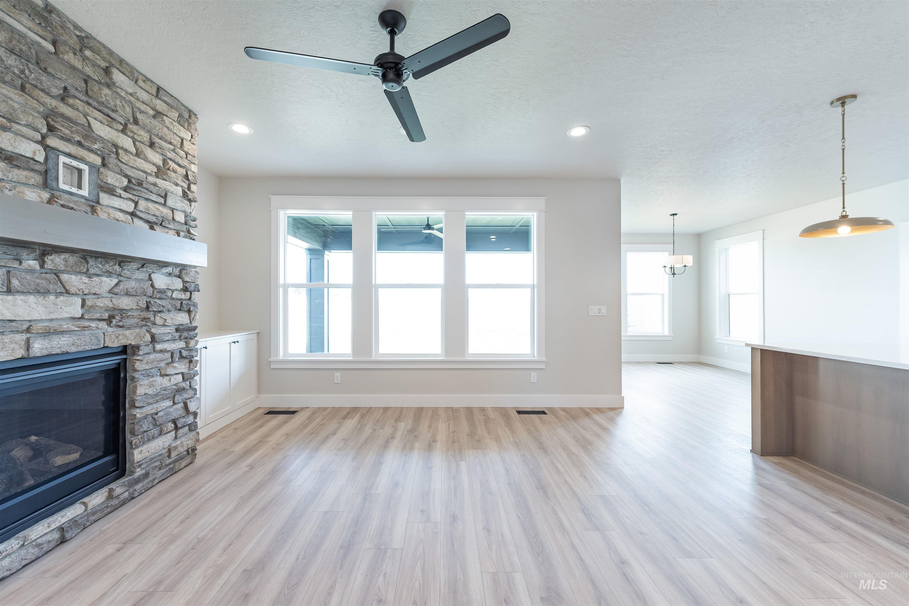 Unfurnished living room with light wood finished floors, a ceiling fan, a stone fireplace, recessed lighting, and a textured ceiling