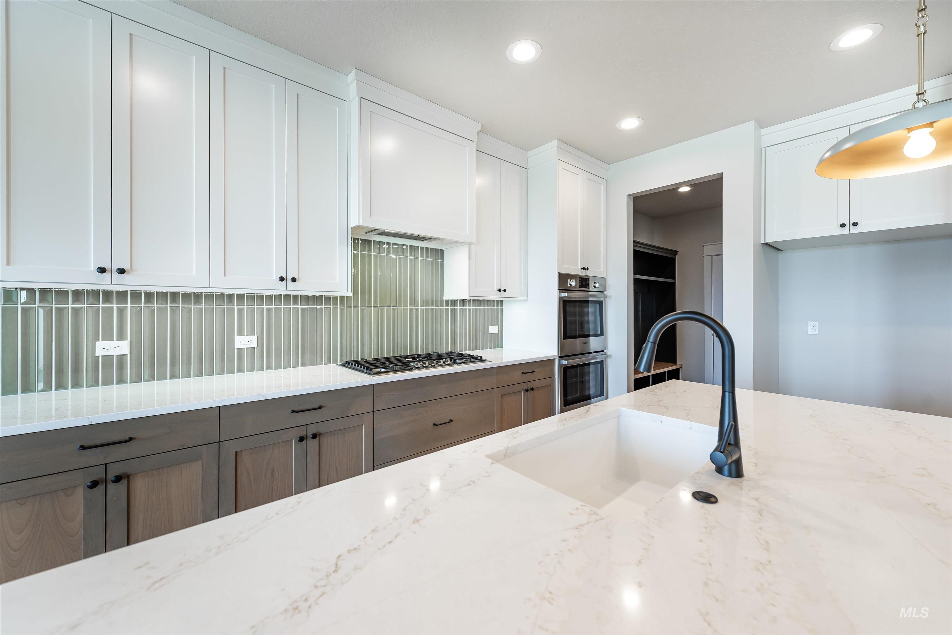 Kitchen featuring white cabinetry, tasteful backsplash, light stone counters, decorative light fixtures, and stainless steel appliances