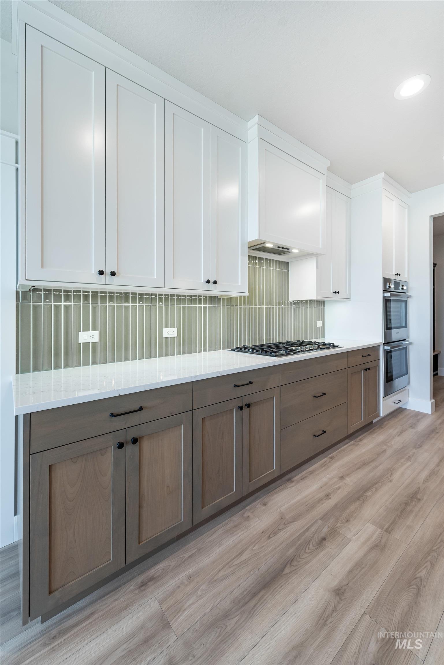 Kitchen with white cabinetry, brown cabinets, light wood finished floors, backsplash, and appliances with stainless steel finishes