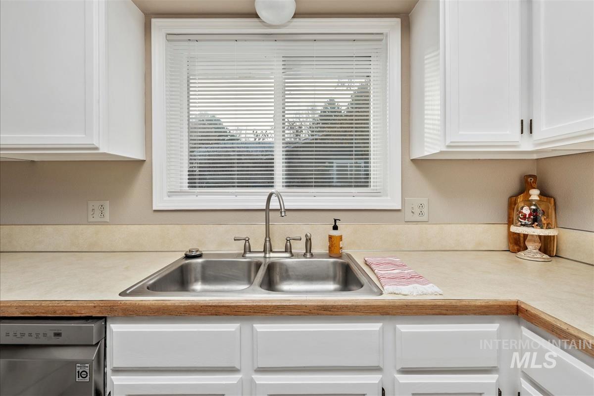 Kitchen featuring light countertops, stainless steel dishwasher, and white cabinets