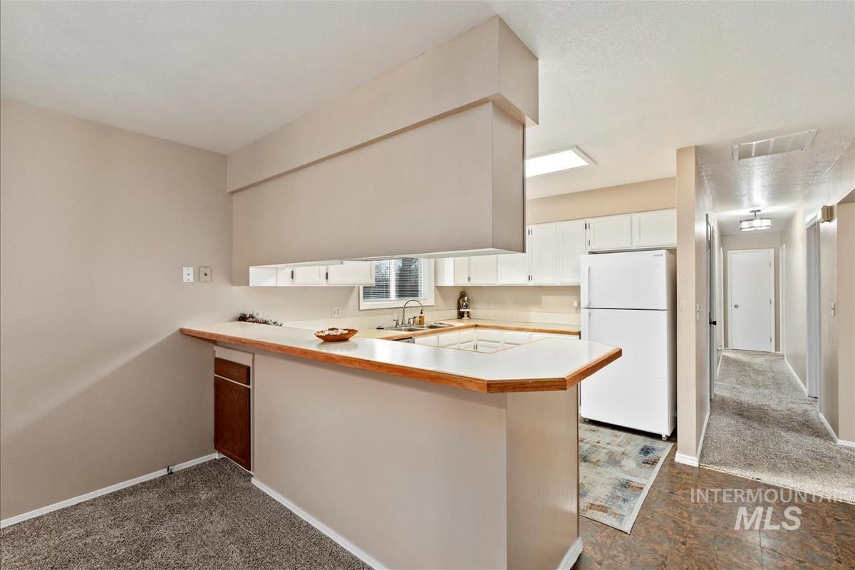 Kitchen featuring light countertops, freestanding refrigerator, dark carpet, and a peninsula