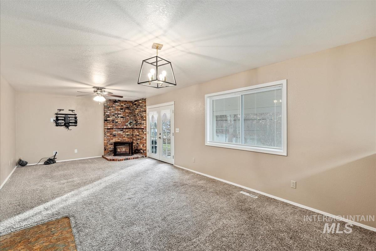 Unfurnished living room featuring a textured ceiling, carpet flooring, ceiling fan, a fireplace, and a chandelier