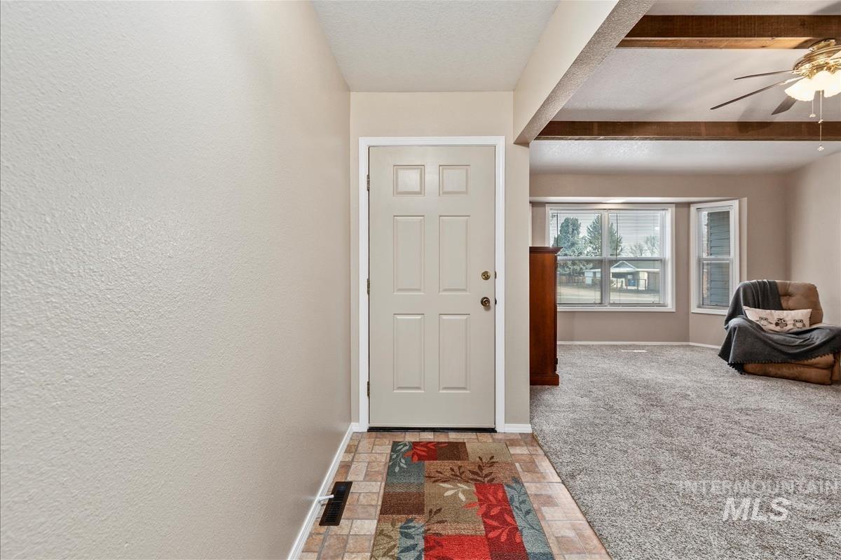 Doorway to outside featuring a ceiling fan, beam ceiling, stone finish floors, and carpet floors
