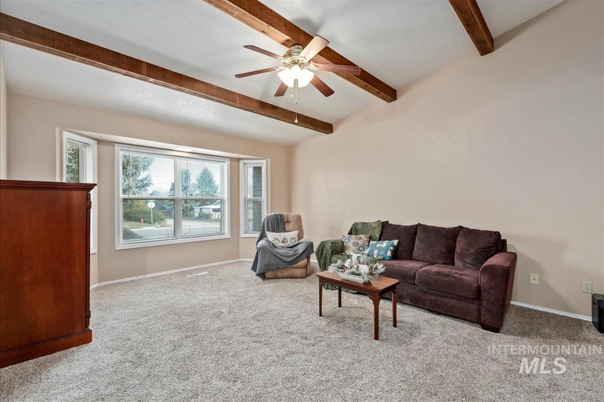Living room with light colored carpet, beam ceiling, and ceiling fan