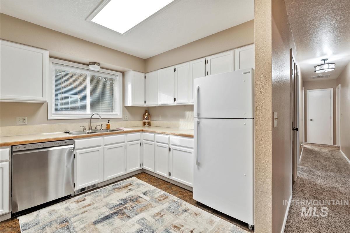Kitchen with white cabinetry, freestanding refrigerator, stainless steel dishwasher, light countertops, and a textured wall