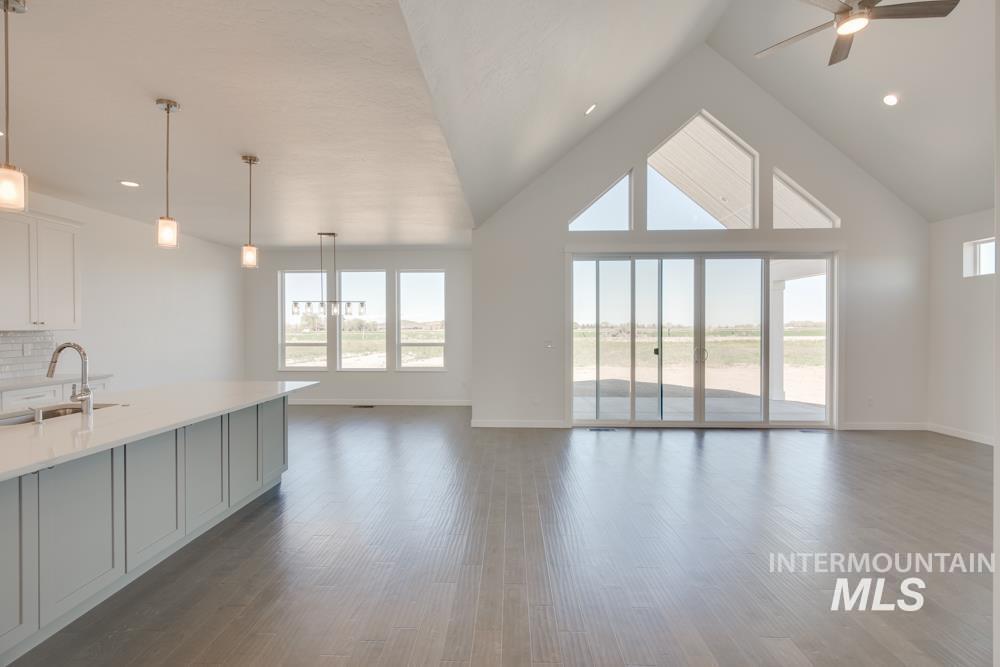 Unfurnished living room with dark wood-style flooring, high vaulted ceiling, a ceiling fan, recessed lighting, and a chandelier
