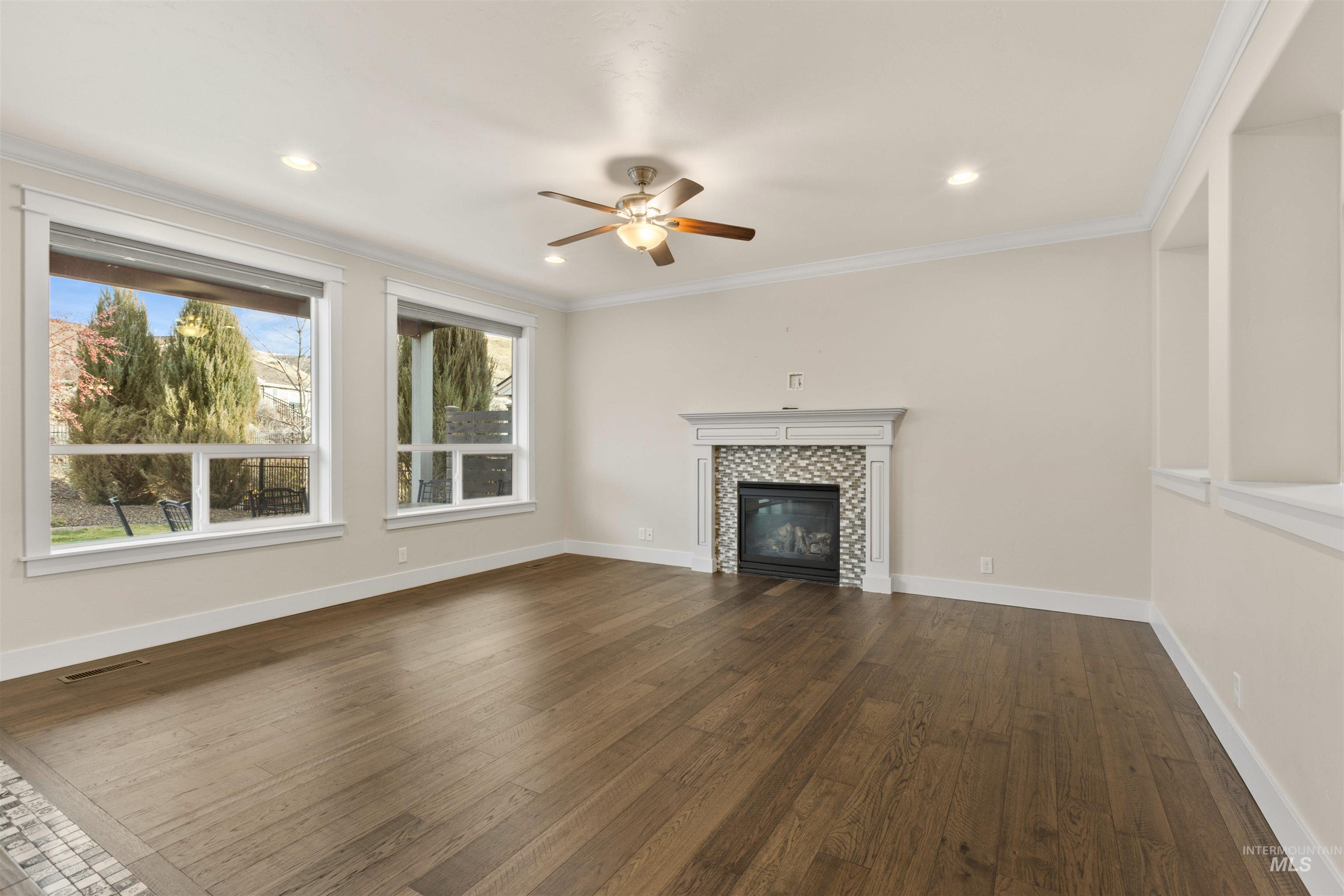 Unfurnished living room featuring dark wood-style flooring, crown molding, a tile fireplace, a ceiling fan, and recessed lighting