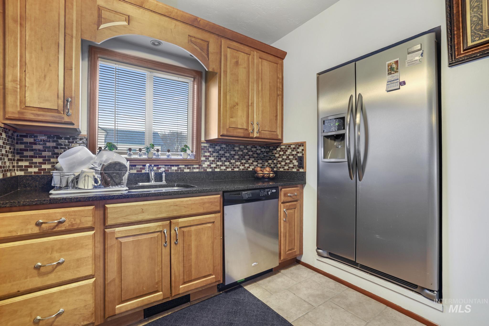 Kitchen with stainless steel appliances, brown cabinetry, tasteful backsplash, and light tile patterned floors