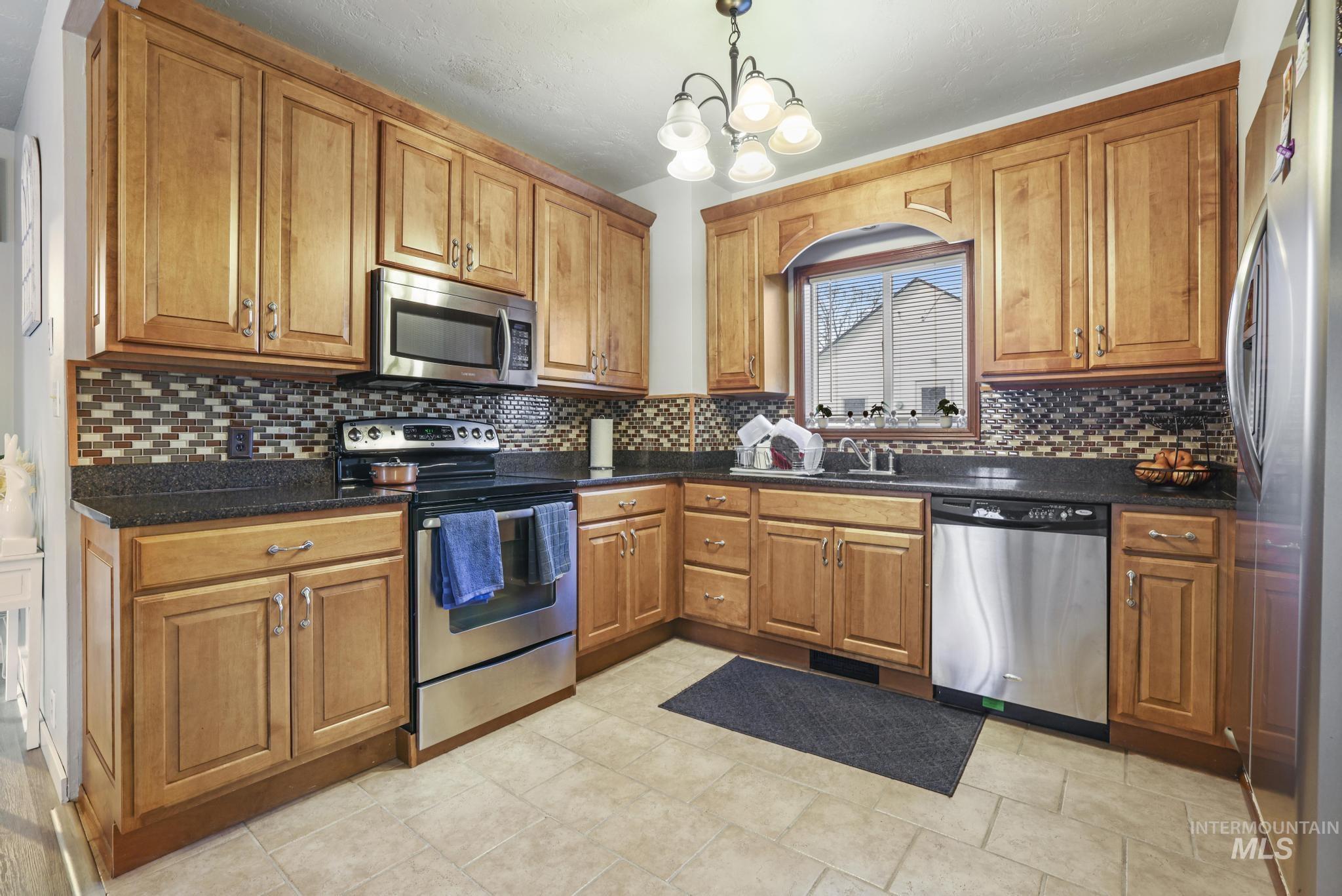 Kitchen with appliances with stainless steel finishes, brown cabinetry, and hanging light fixtures