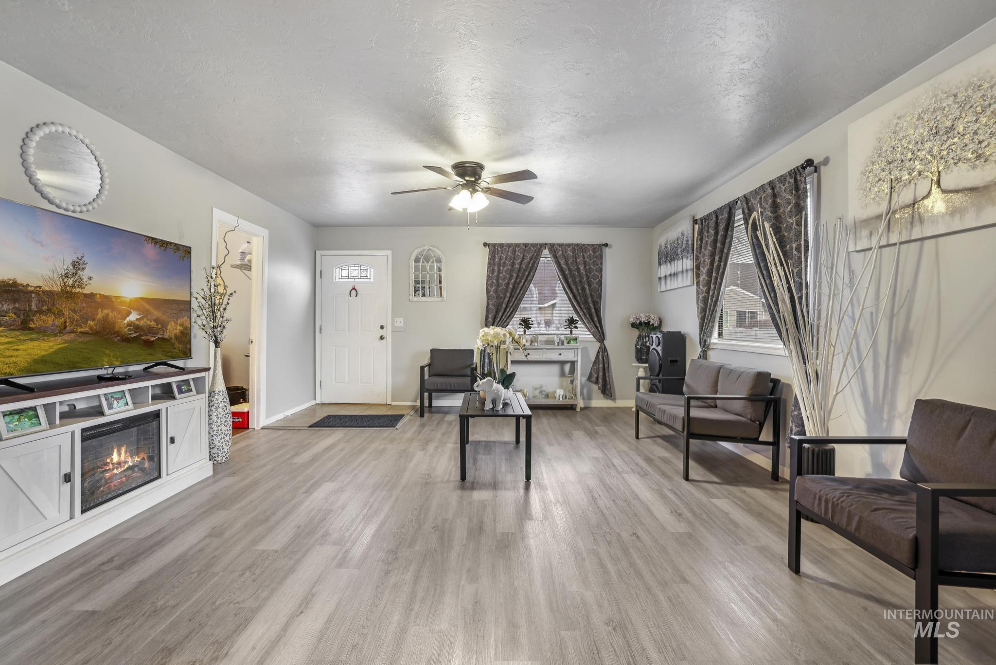 Living room featuring a ceiling fan, light wood-style flooring, a glass covered fireplace, and a textured ceiling