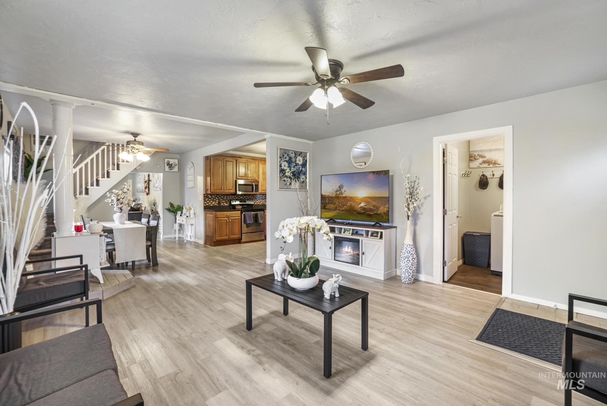Living room featuring a ceiling fan, light wood-type flooring, decorative columns, stairway, and a glass covered fireplace