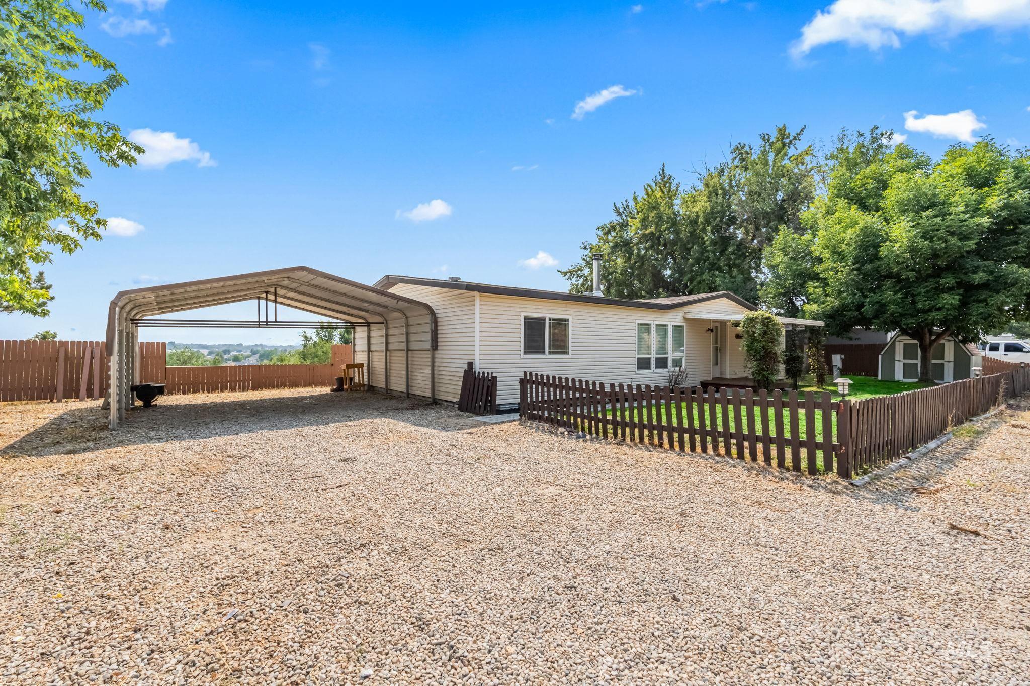 View of front of home with a fenced front yard, gravel driveway, and a detached carport
