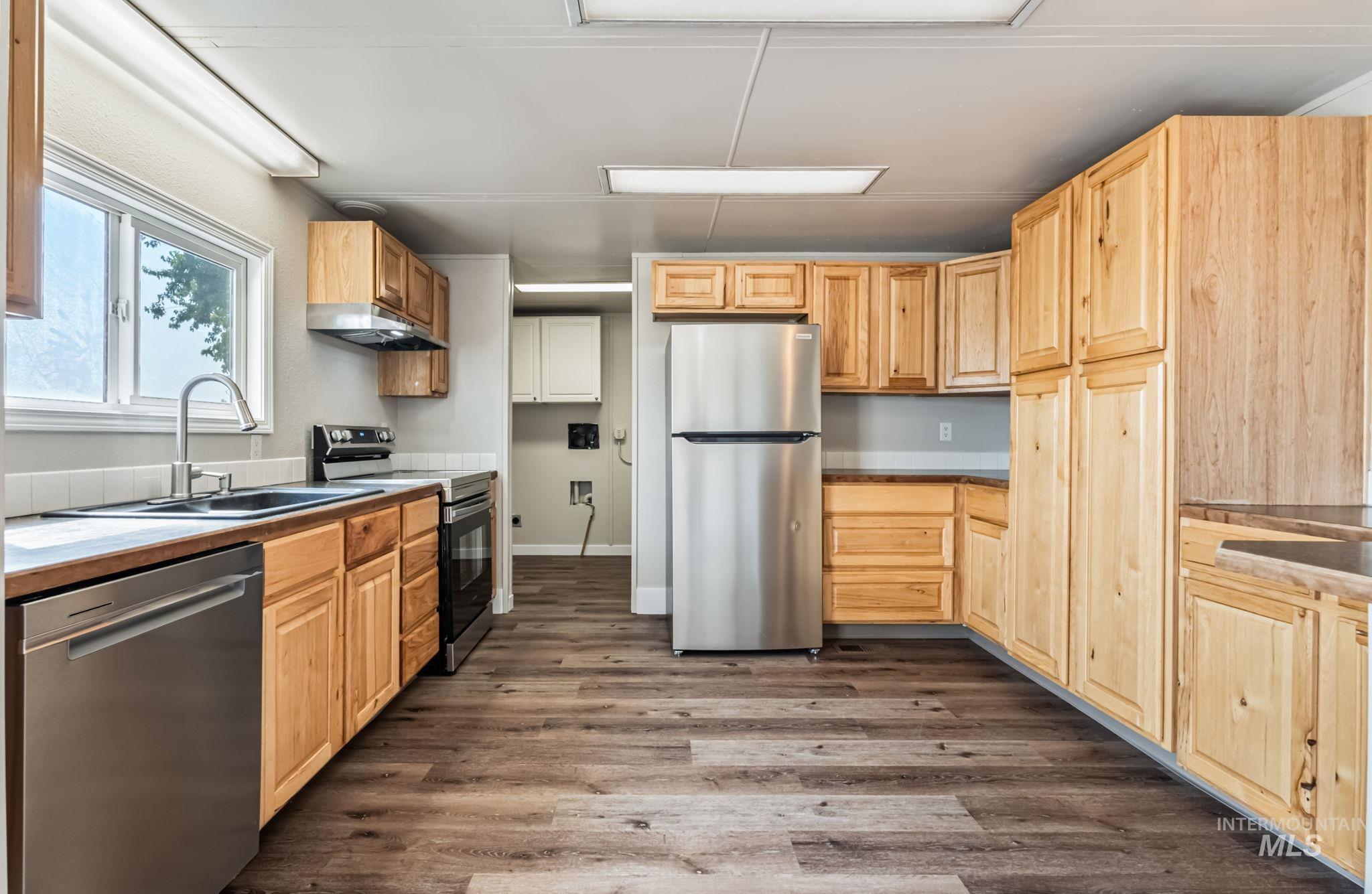 Kitchen with stainless steel appliances, dark wood-style flooring, light brown cabinets, and under cabinet range hood