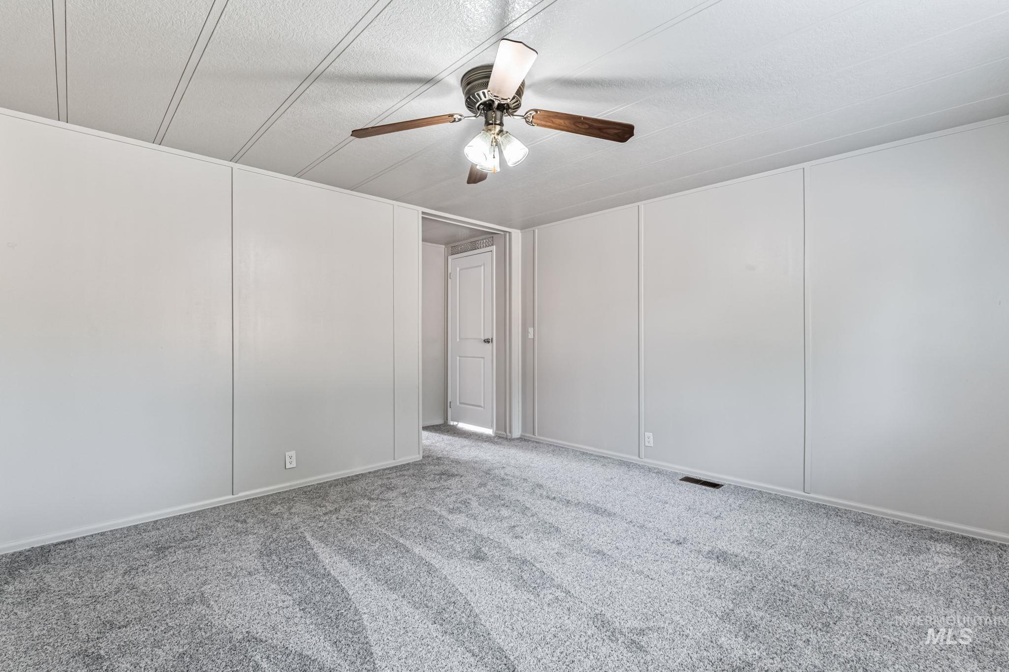 Carpeted spare room featuring ceiling fan and a decorative wall