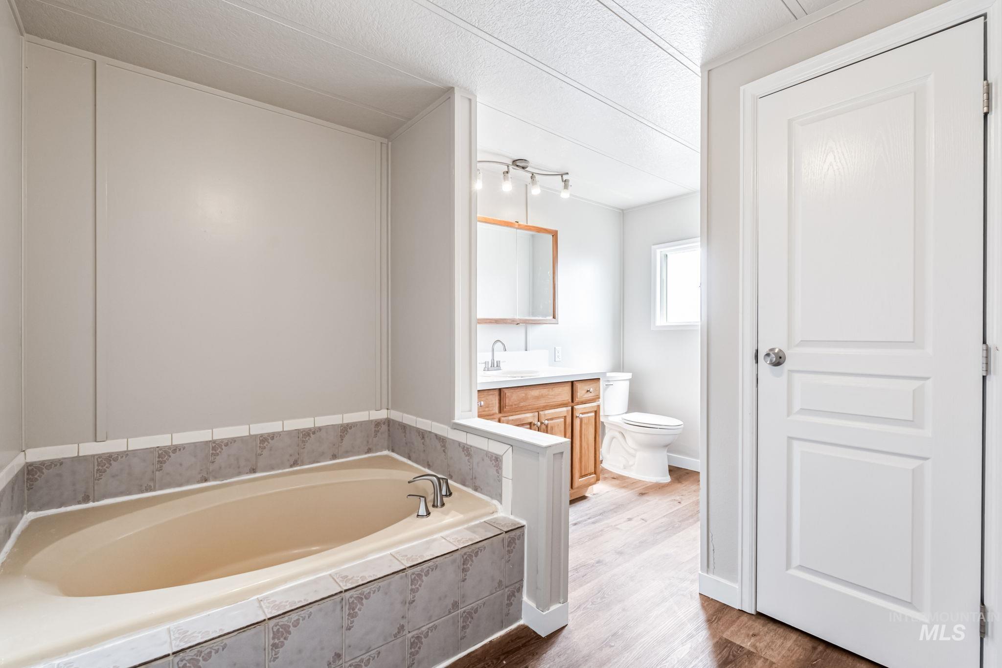 Bathroom with vanity, a bath, wood finished floors, and a textured ceiling