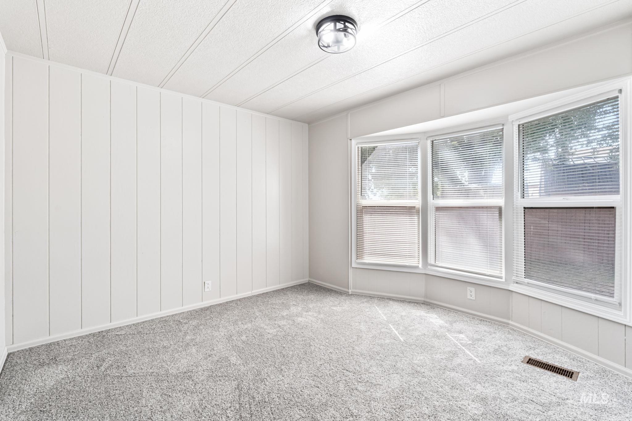 Carpeted spare room featuring wooden walls and baseboards