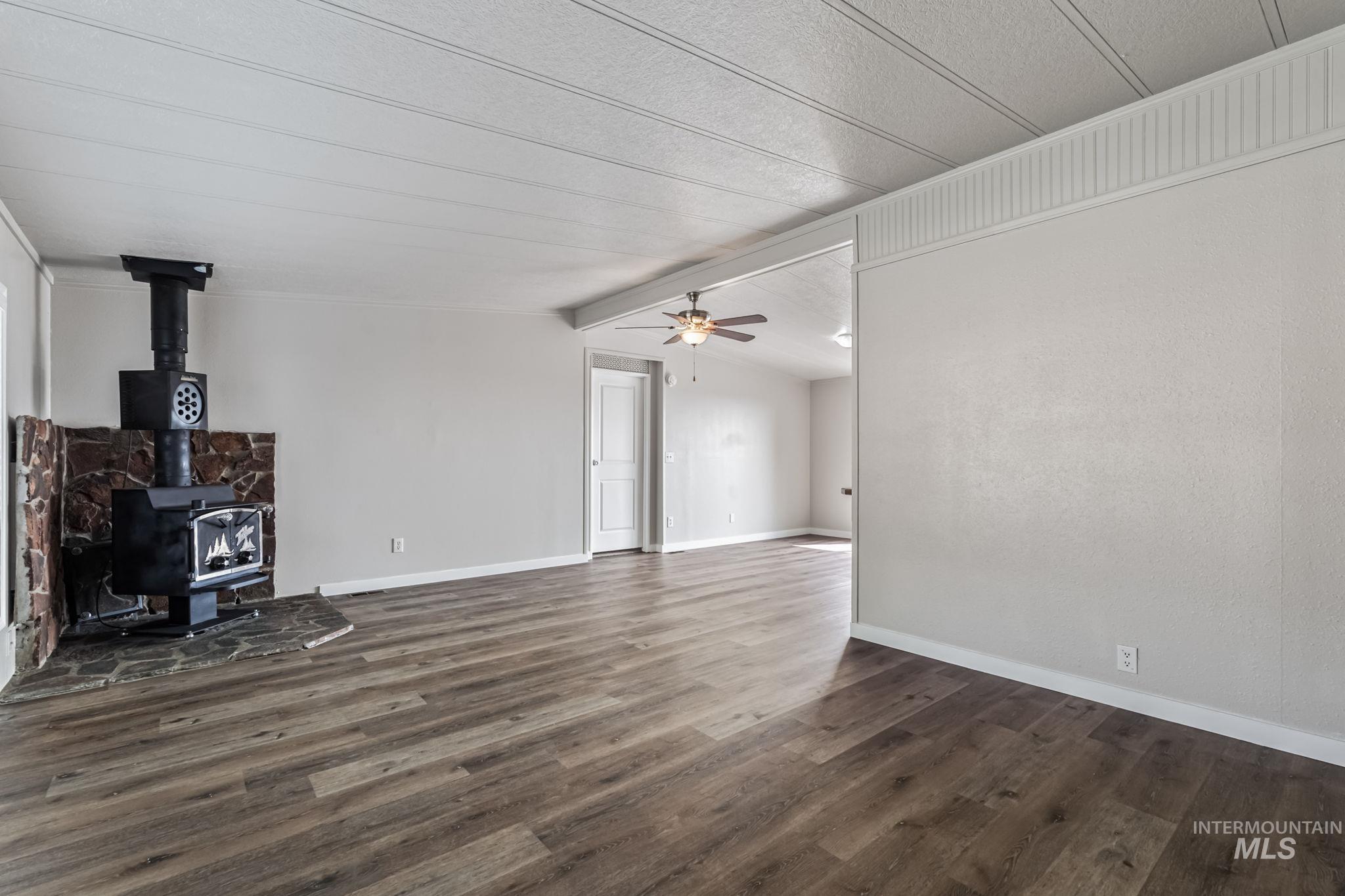 Unfurnished living room featuring a wood stove, dark wood-style floors, and a ceiling fan