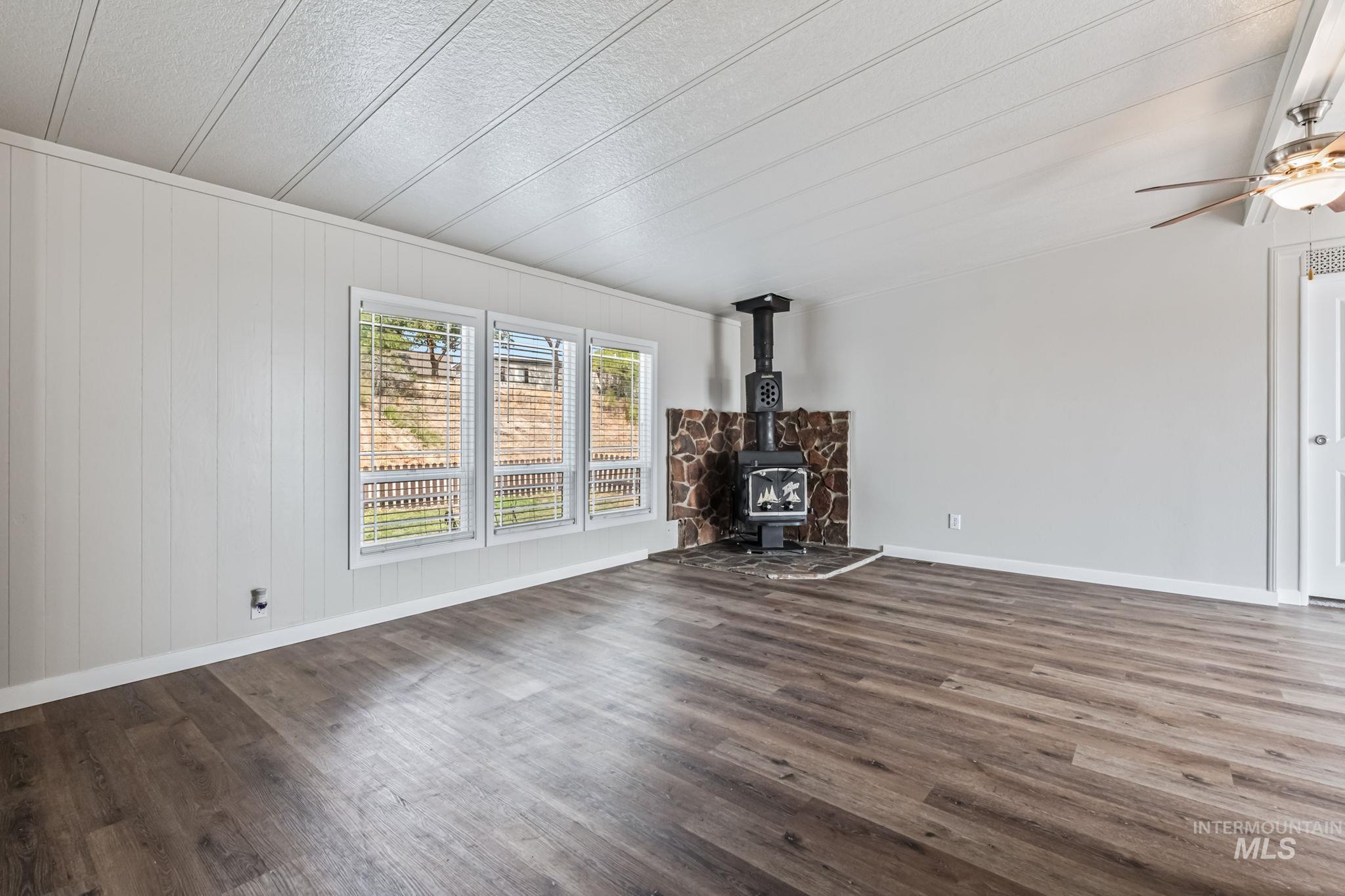 Unfurnished living room with a wood stove, wood finished floors, and wood walls