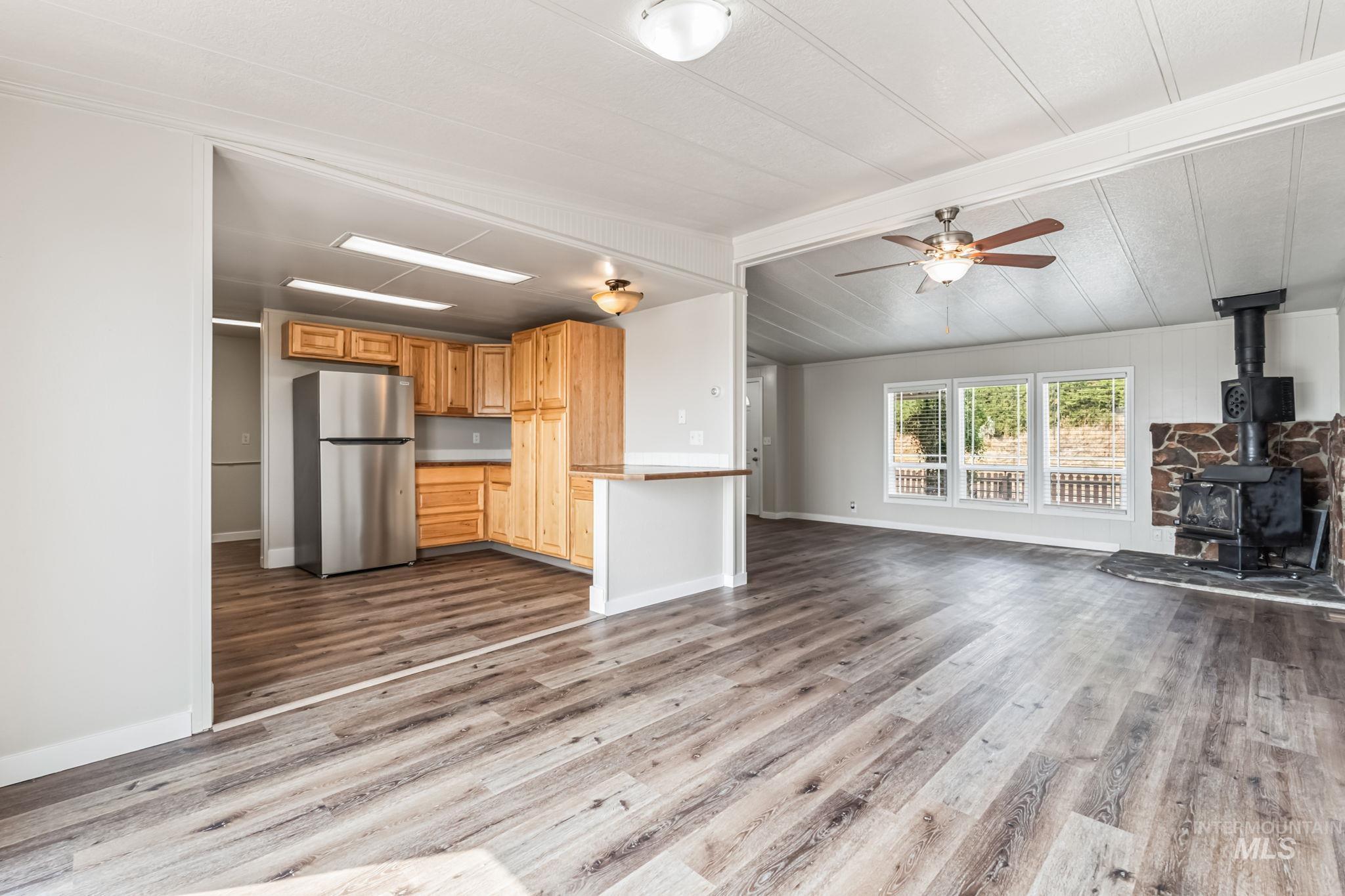 Kitchen featuring open floor plan, freestanding refrigerator, a wood stove, dark wood finished floors, and light countertops
