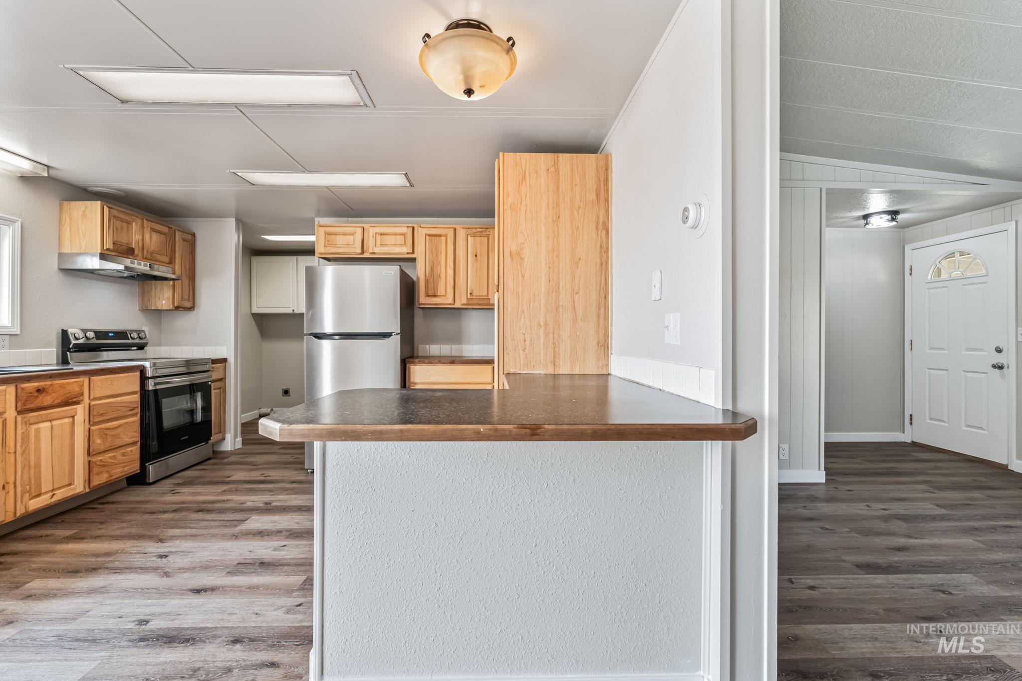 Kitchen featuring dark wood-style flooring, stainless steel appliances, dark countertops, a peninsula, and under cabinet range hood