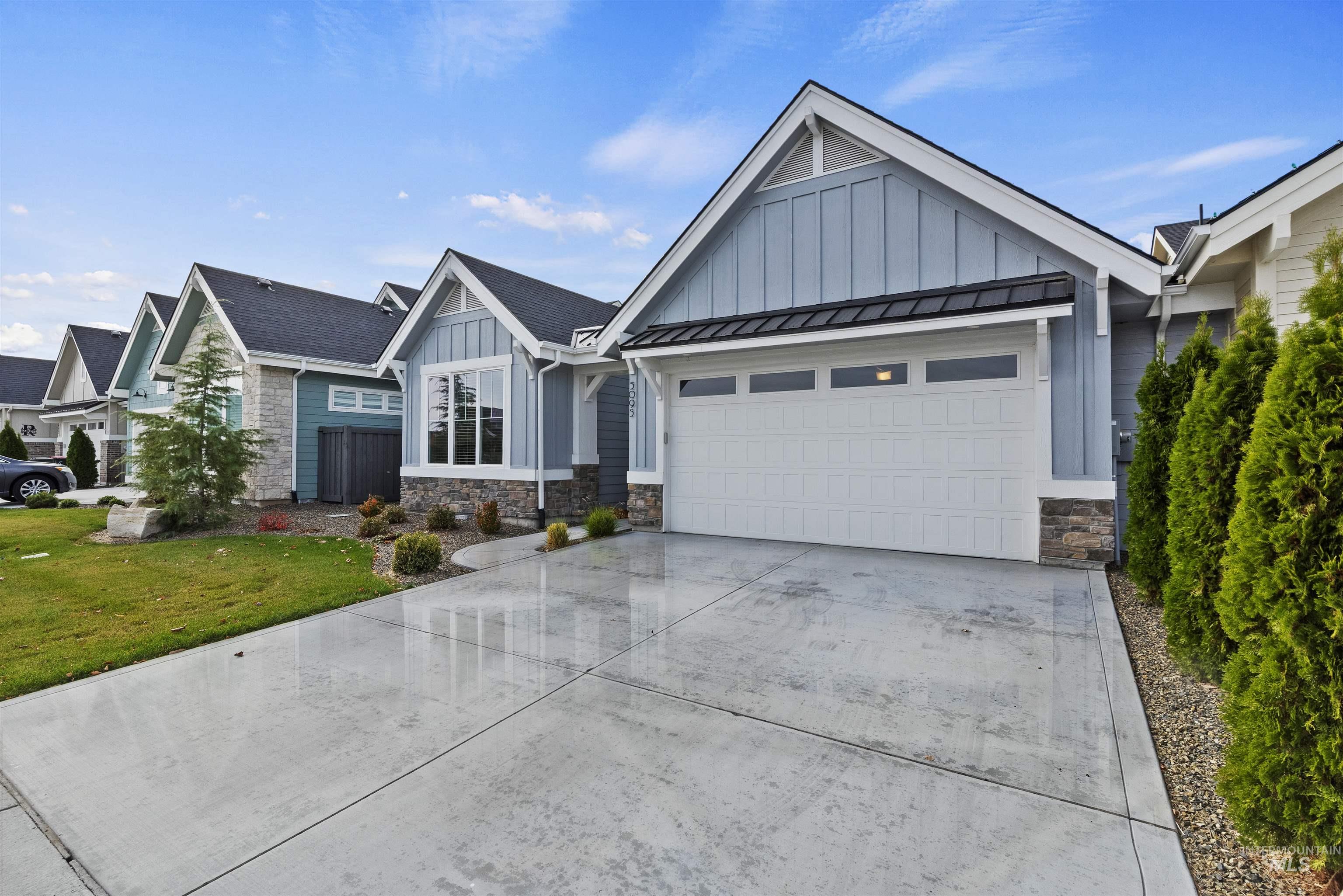 View of front of home featuring board and batten siding, stone siding, concrete driveway, a garage, and a front yard