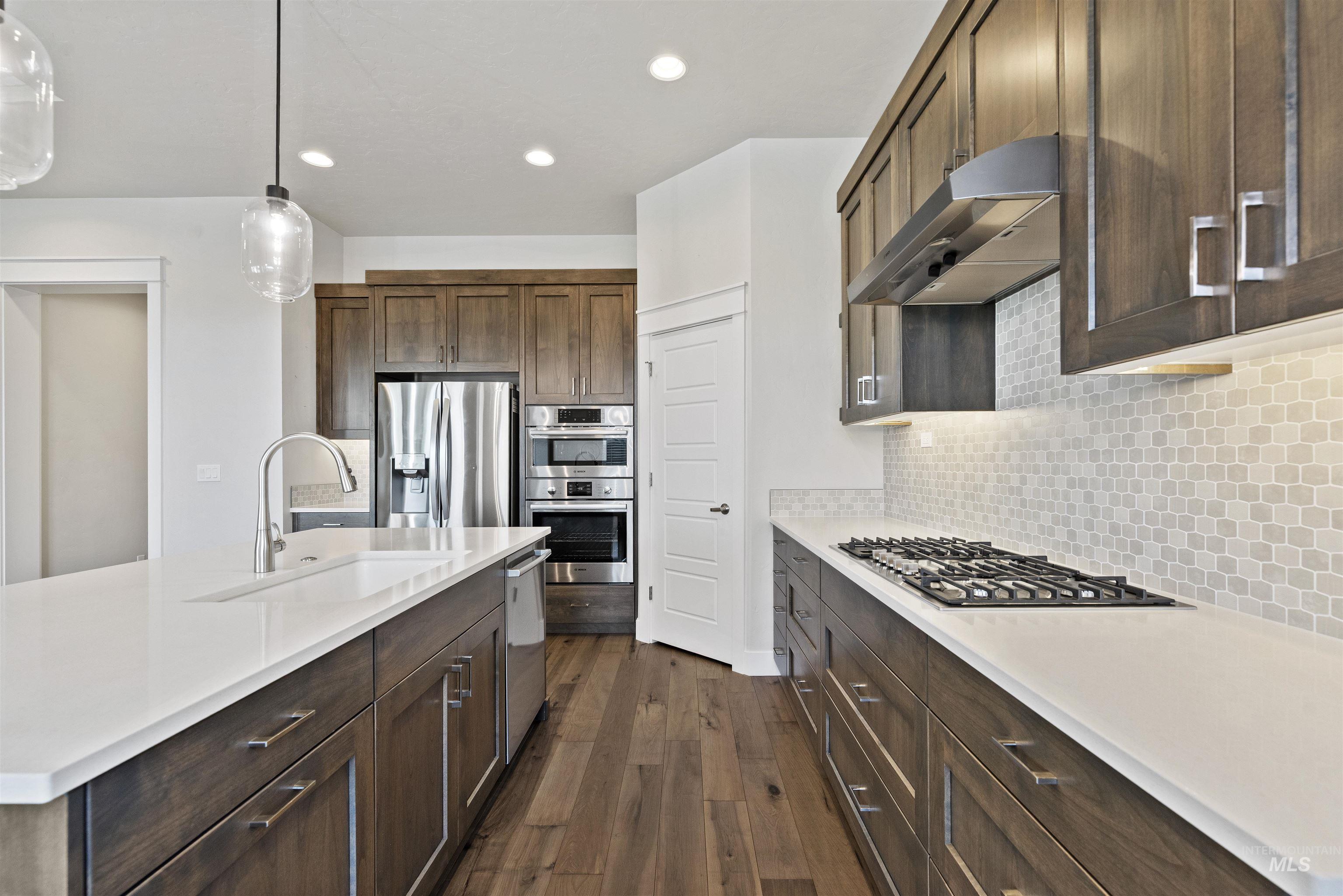 Kitchen with decorative light fixtures, dark brown cabinets, decorative backsplash, appliances with stainless steel finishes, and under cabinet range hood