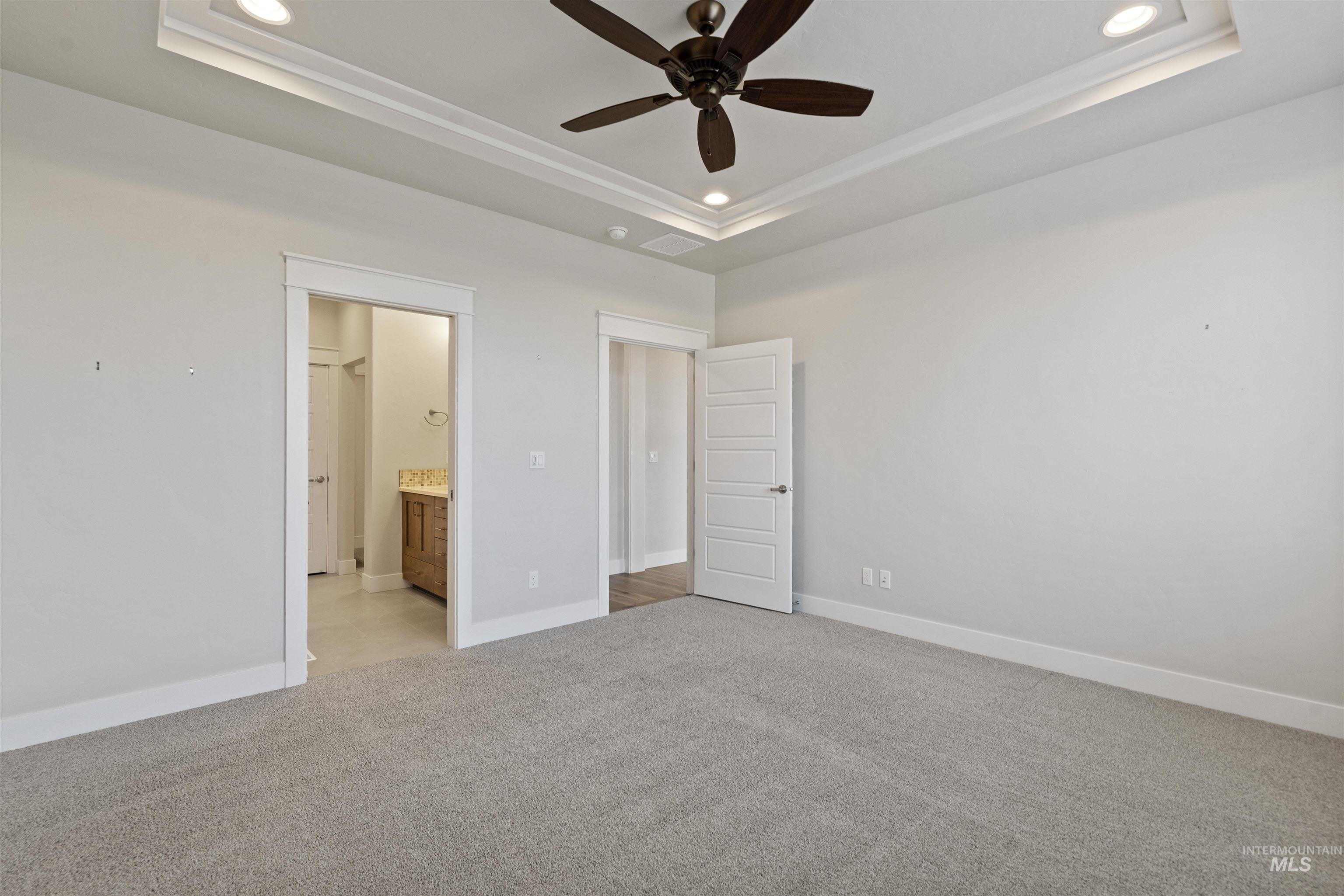 Unfurnished bedroom featuring recessed lighting, light carpet, connected bathroom, ceiling fan, and a raised ceiling