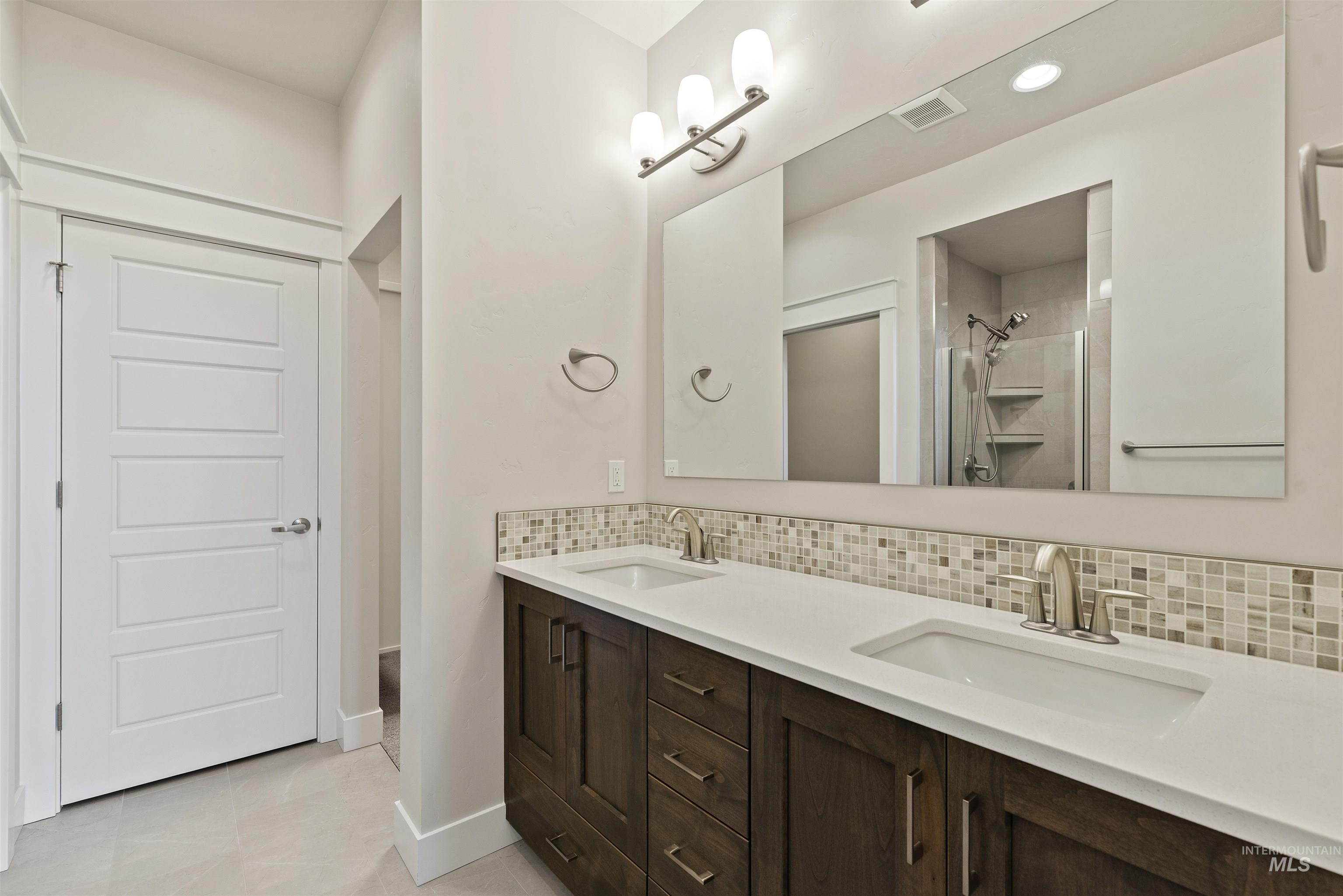 Bathroom featuring tasteful backsplash, double vanity, a shower stall, light tile patterned flooring, and recessed lighting