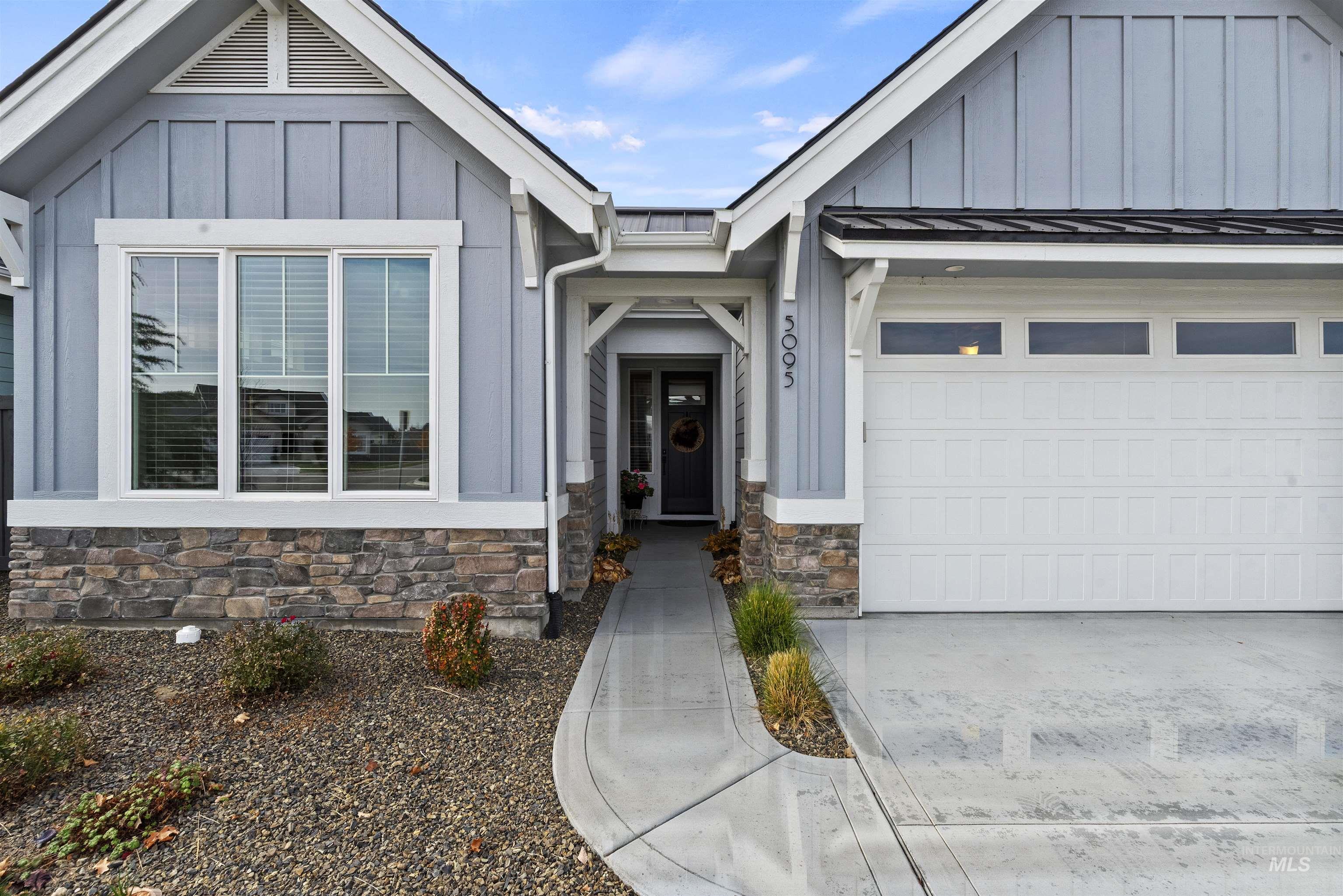 Entrance to property with board and batten siding, driveway, a garage, a metal roof, and stone siding