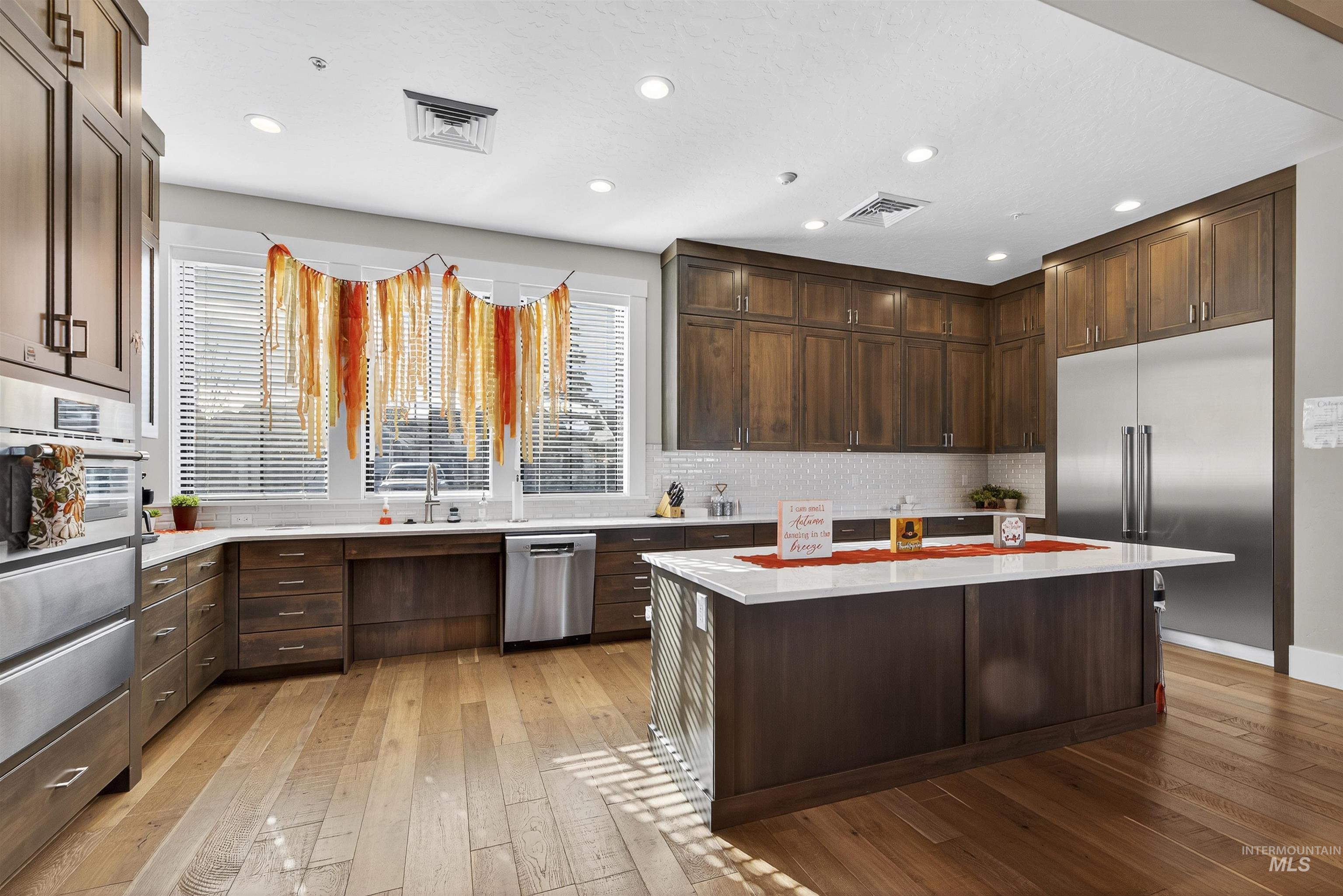 Kitchen featuring dark brown cabinets, appliances with stainless steel finishes, a center island, light wood-style flooring, and recessed lighting