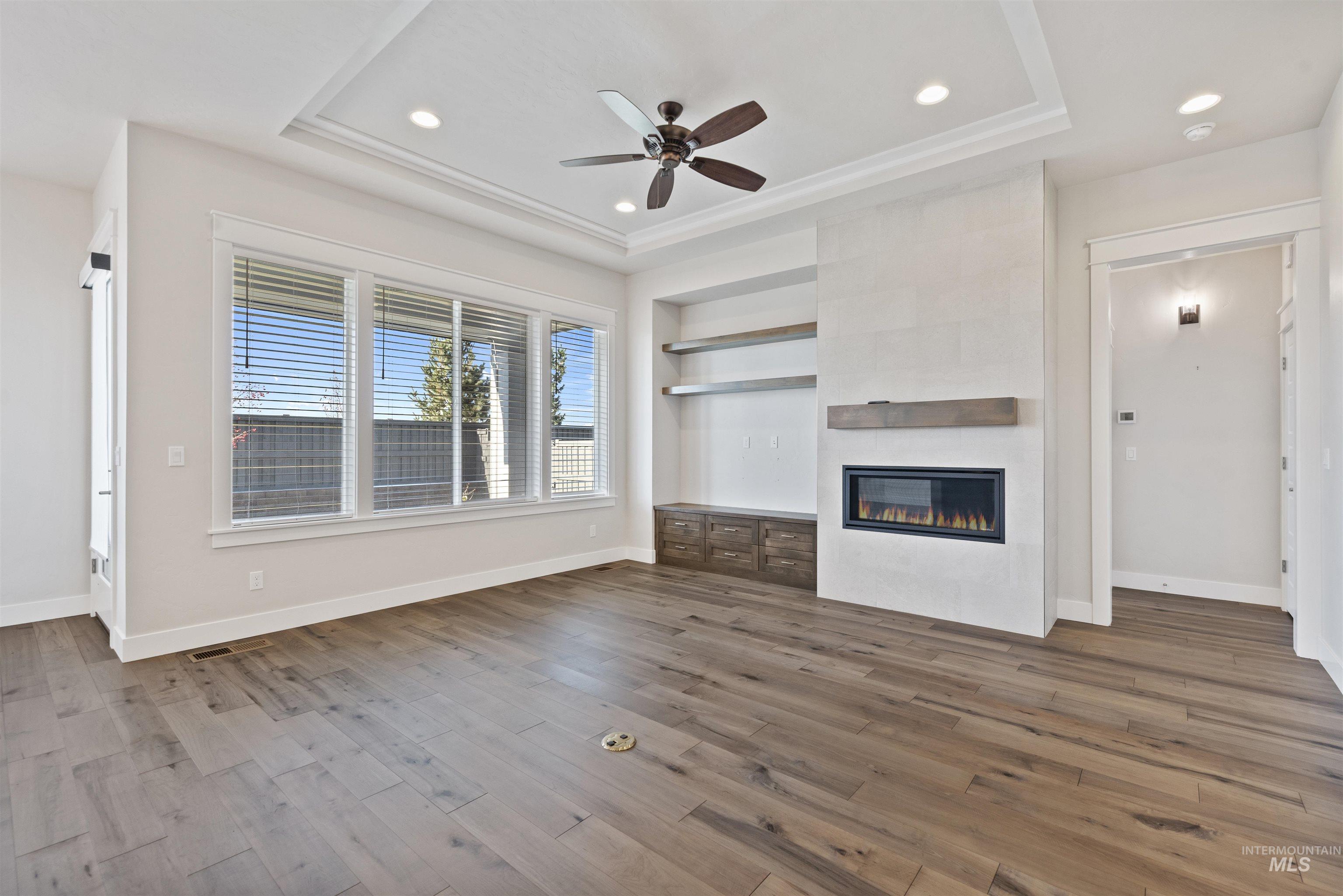 Unfurnished living room featuring dark wood-type flooring, a raised ceiling, a tile fireplace, a ceiling fan, and recessed lighting