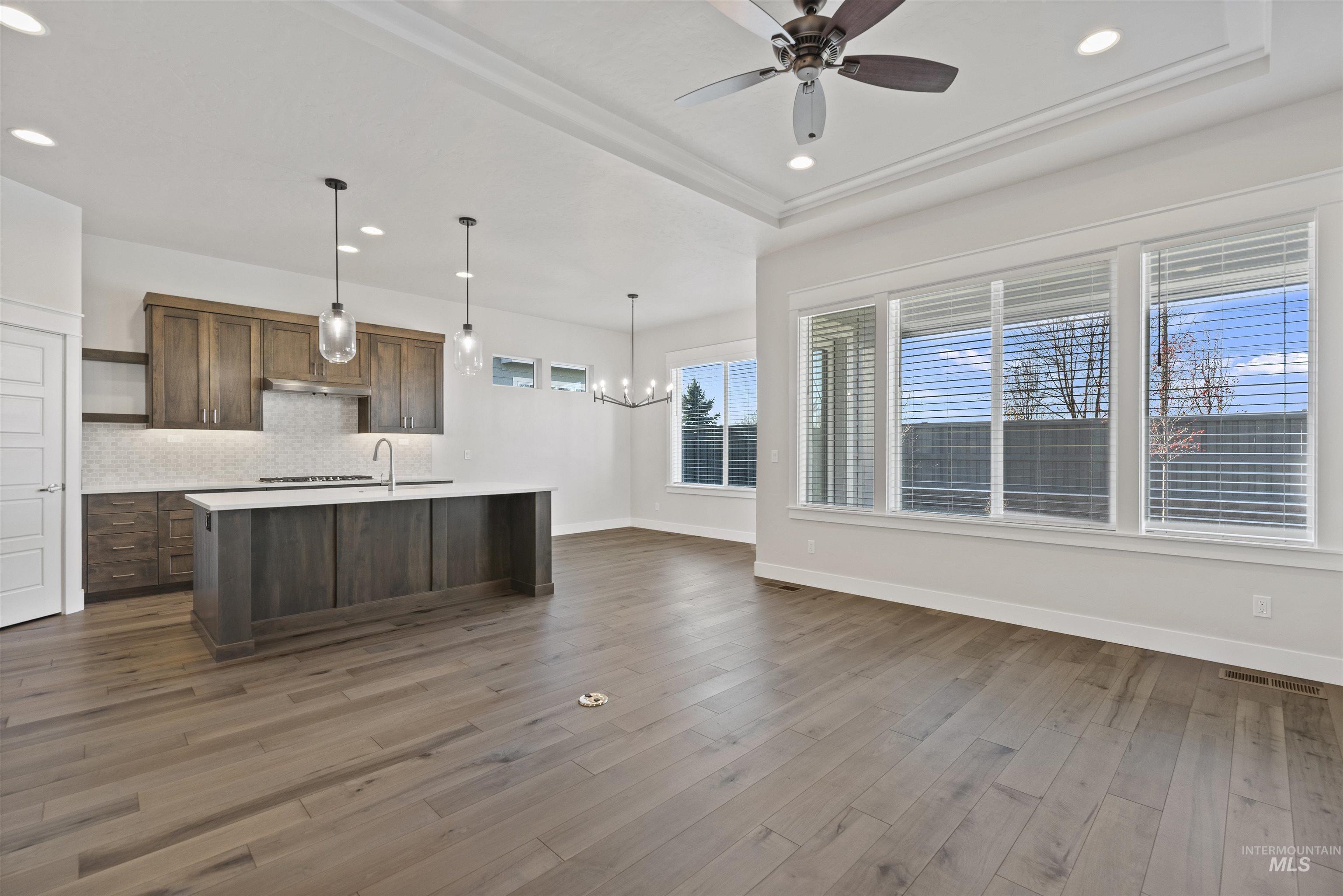 Kitchen featuring hanging light fixtures, recessed lighting, dark wood finished floors, a kitchen island with sink, and decorative backsplash