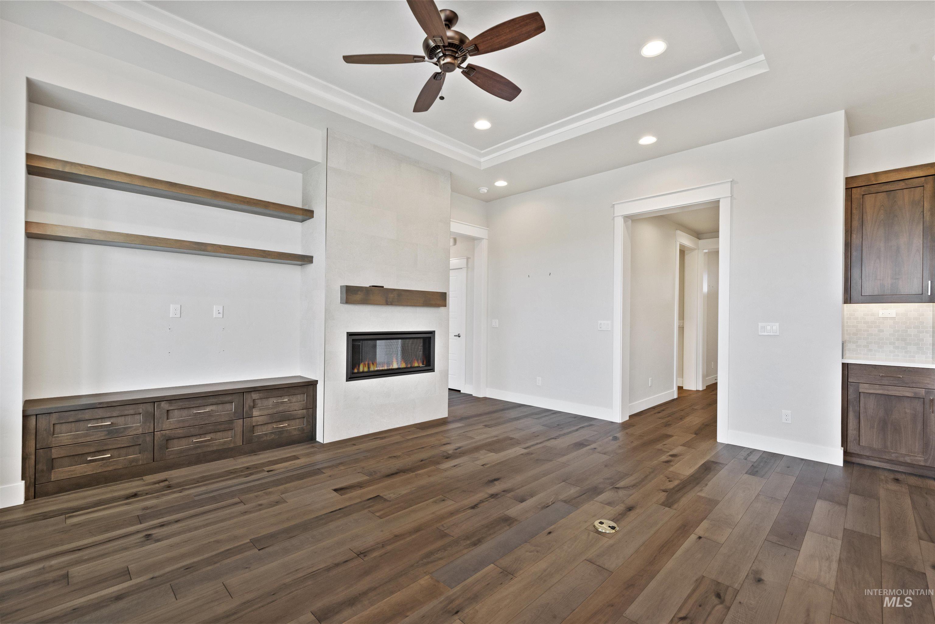 Unfurnished living room featuring recessed lighting, dark wood-type flooring, ceiling fan, a tiled fireplace, and a tray ceiling