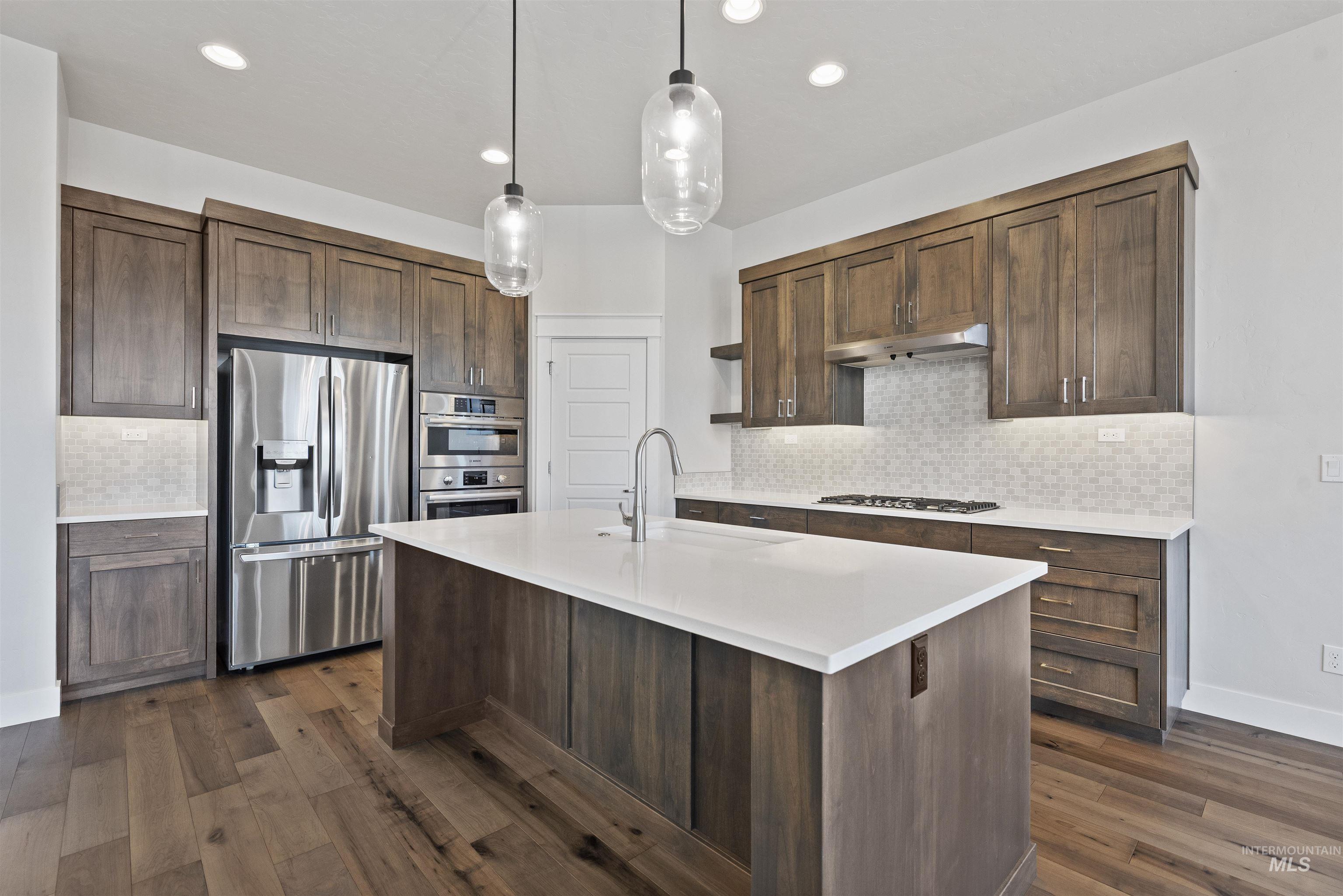 Kitchen with backsplash, stainless steel appliances, hanging light fixtures, a kitchen island with sink, and recessed lighting