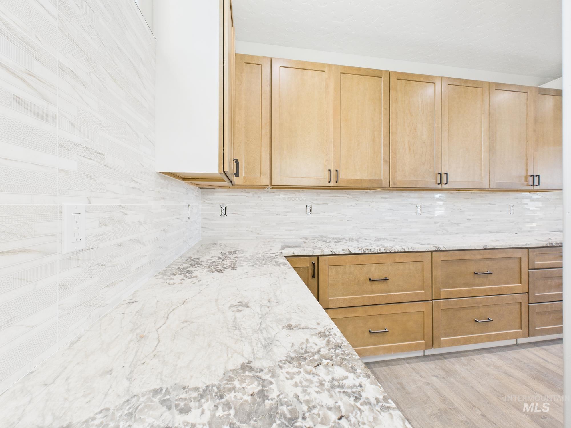 Kitchen with light brown cabinetry, light stone countertops, light wood-style floors, and decorative backsplash