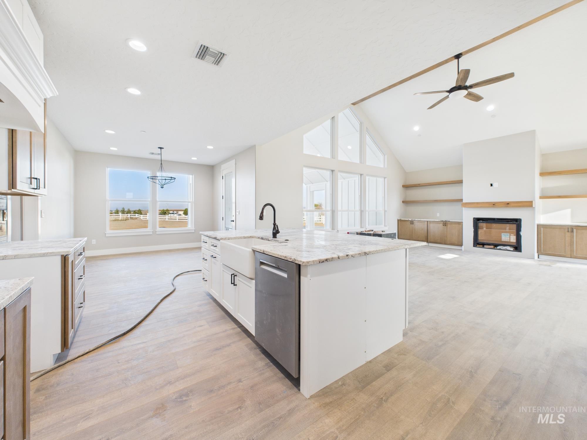 Kitchen featuring open floor plan, an island with sink, light wood finished floors, dishwasher, and high vaulted ceiling