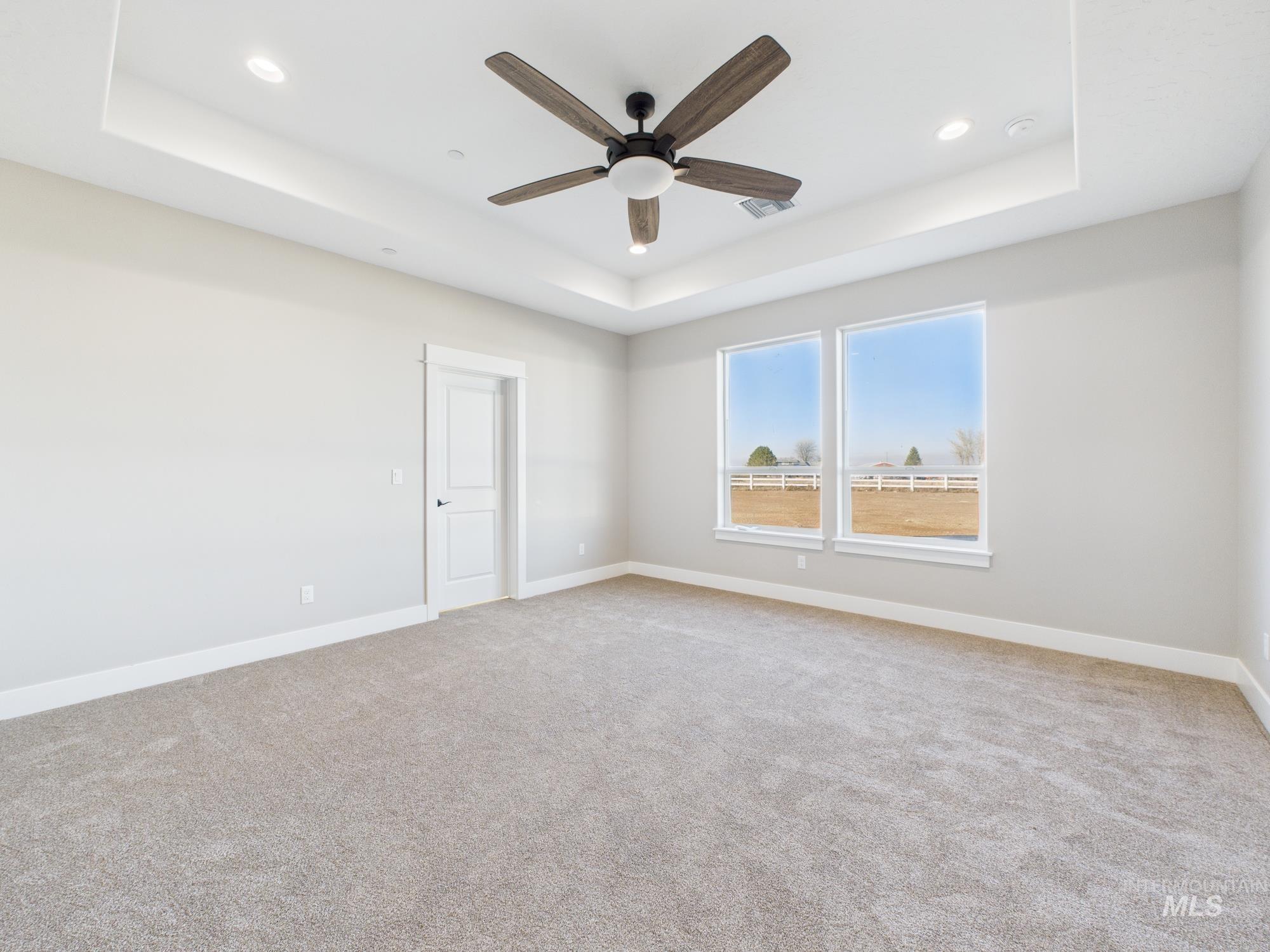 Spare room featuring a tray ceiling, light colored carpet, a ceiling fan, and recessed lighting