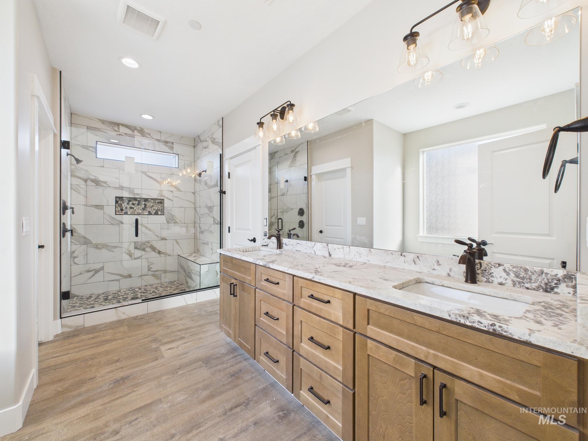 Full bathroom featuring double vanity, a marble finish shower, and light wood-style floors