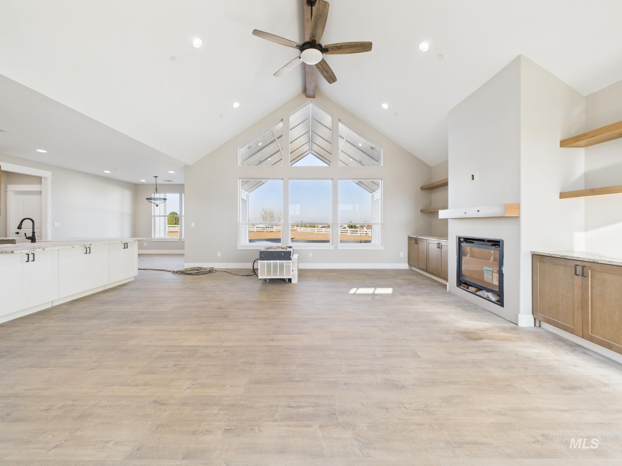 Unfurnished living room featuring high vaulted ceiling, beamed ceiling, ceiling fan, light wood-type flooring, and a glass covered fireplace