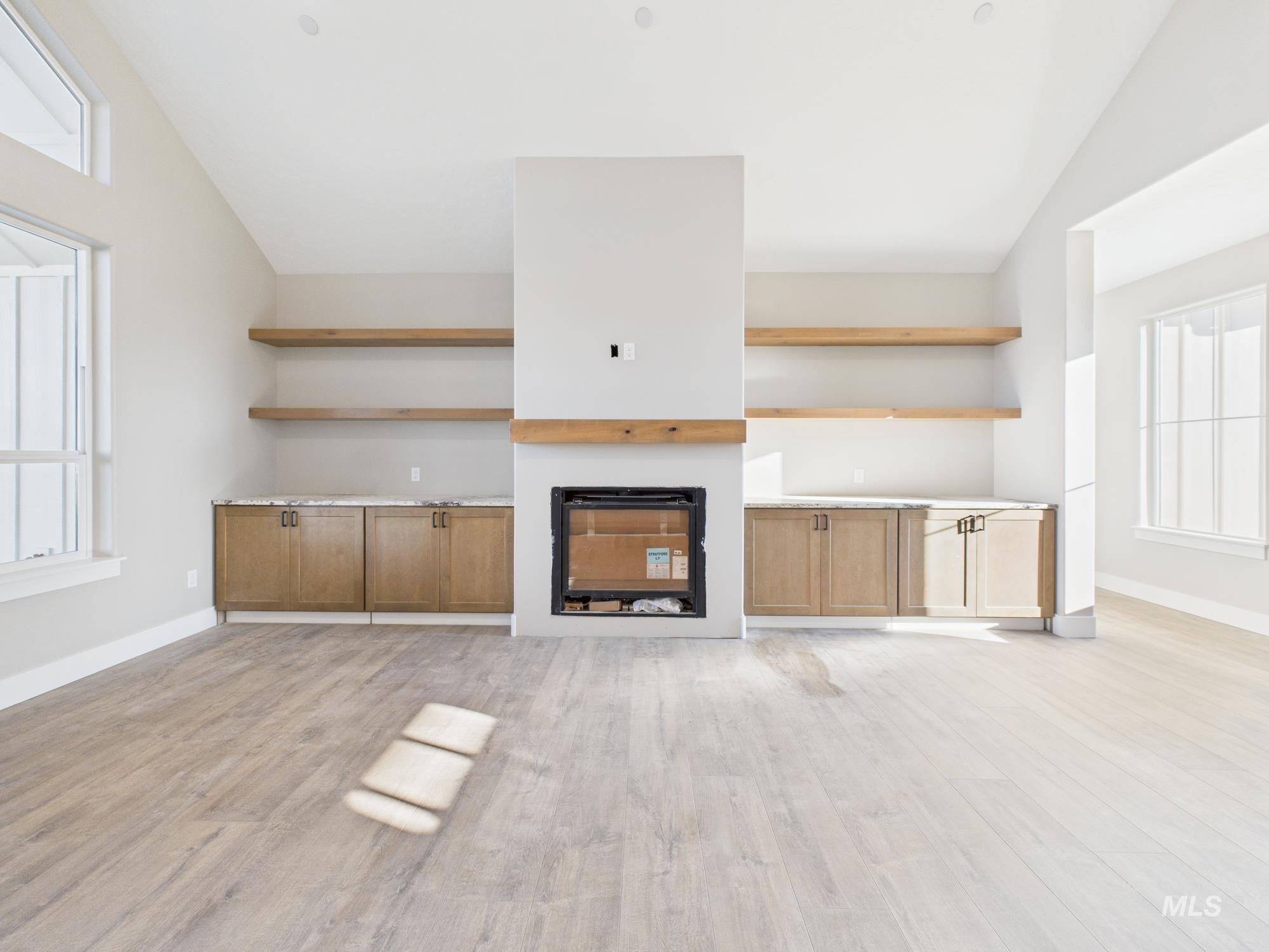 Unfurnished living room featuring vaulted ceiling, a fireplace, and light wood finished floors