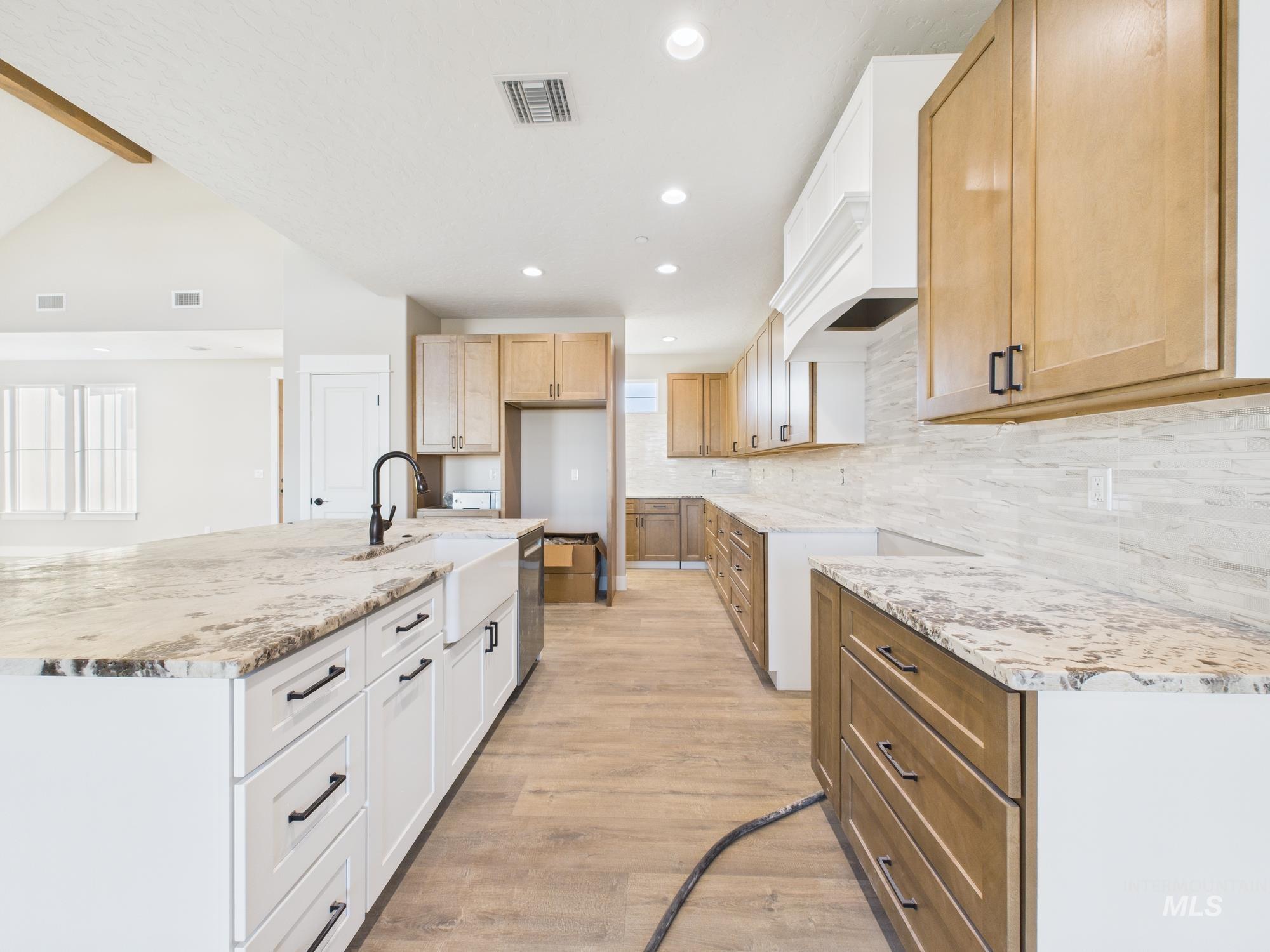 Kitchen featuring a kitchen island with sink, light stone counters, recessed lighting, light wood-style flooring, and vaulted ceiling