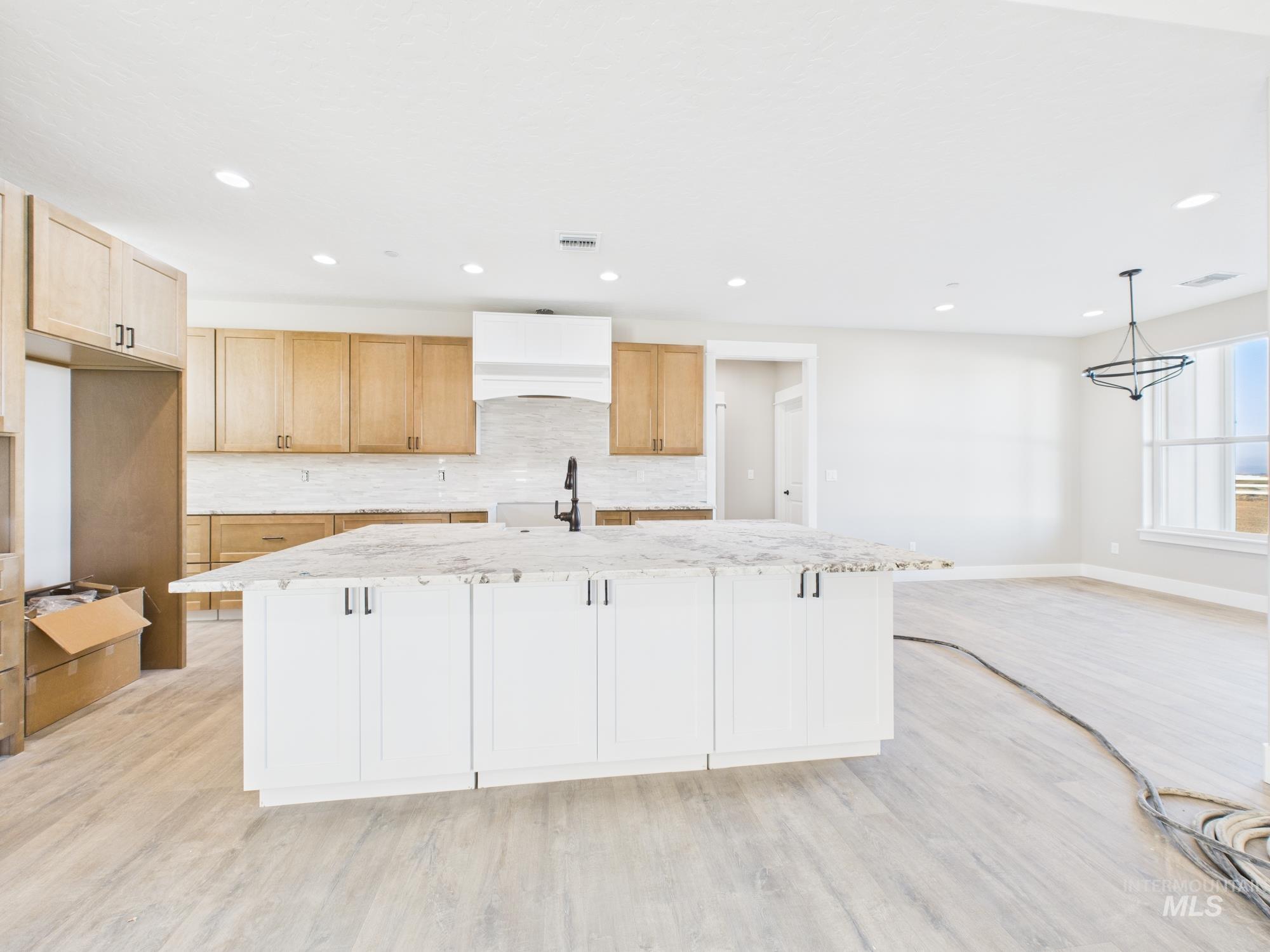 Kitchen featuring a center island with sink, light stone counters, tasteful backsplash, light wood finished floors, and recessed lighting