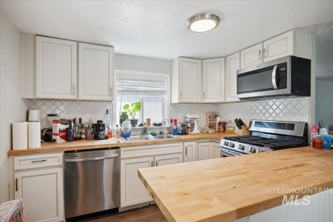 Kitchen with stainless steel appliances, butcher block counters, a peninsula, tasteful backsplash, and white cabinets