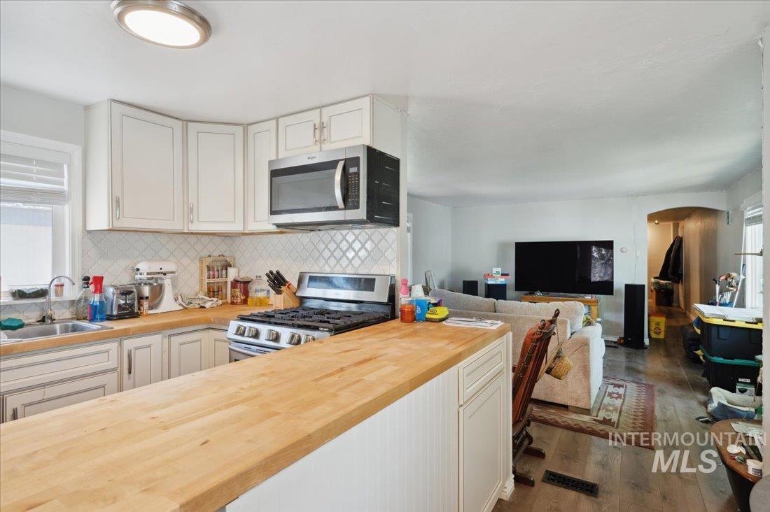 Kitchen featuring appliances with stainless steel finishes, butcher block counters, dark wood-style flooring, decorative backsplash, and white cabinetry