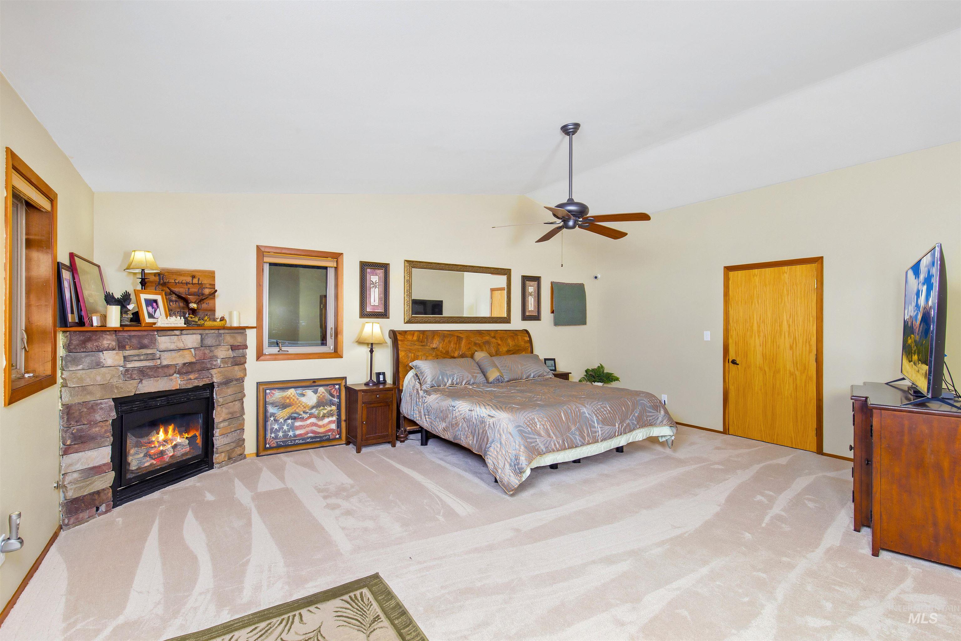 Main Bedroom with vaulted ceiling, carpet flooring, ceiling fan, and a stone fireplace