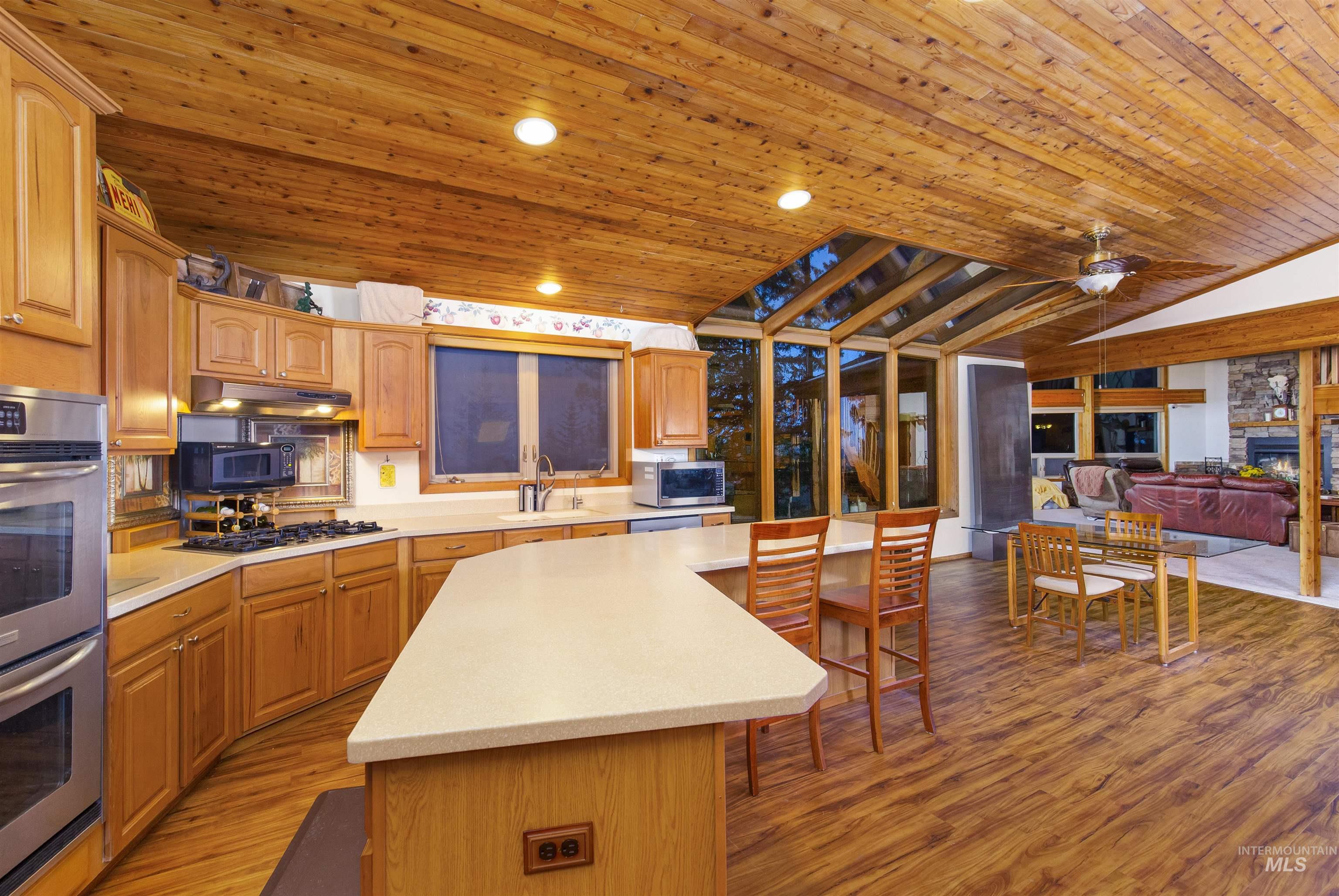 Kitchen featuring wooden ceiling, a kitchen island, appliances with stainless steel finishes, light wood-type flooring, and open floor plan