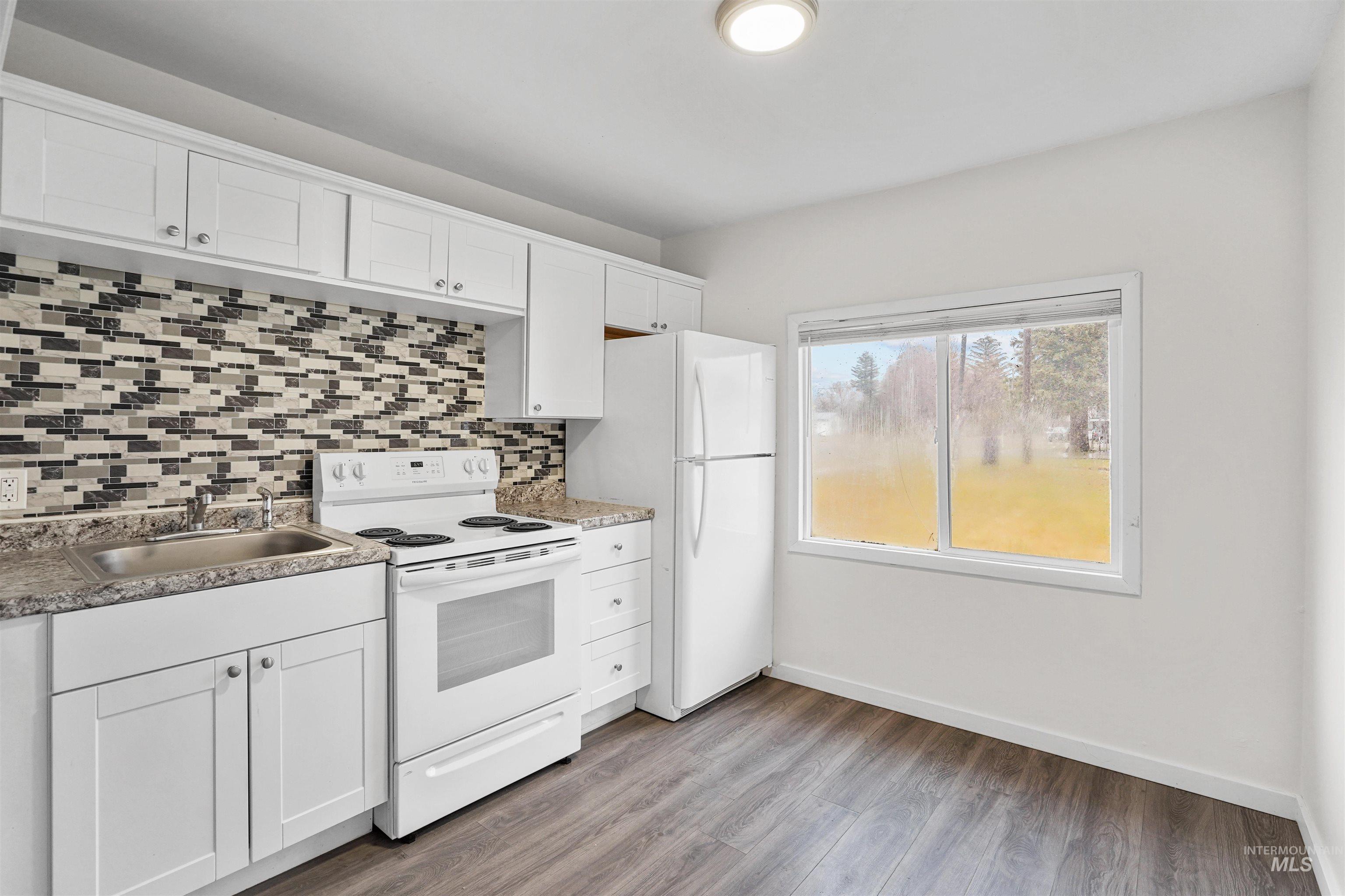 Kitchen featuring white appliances, white cabinets, light wood finished floors, and tasteful backsplash
