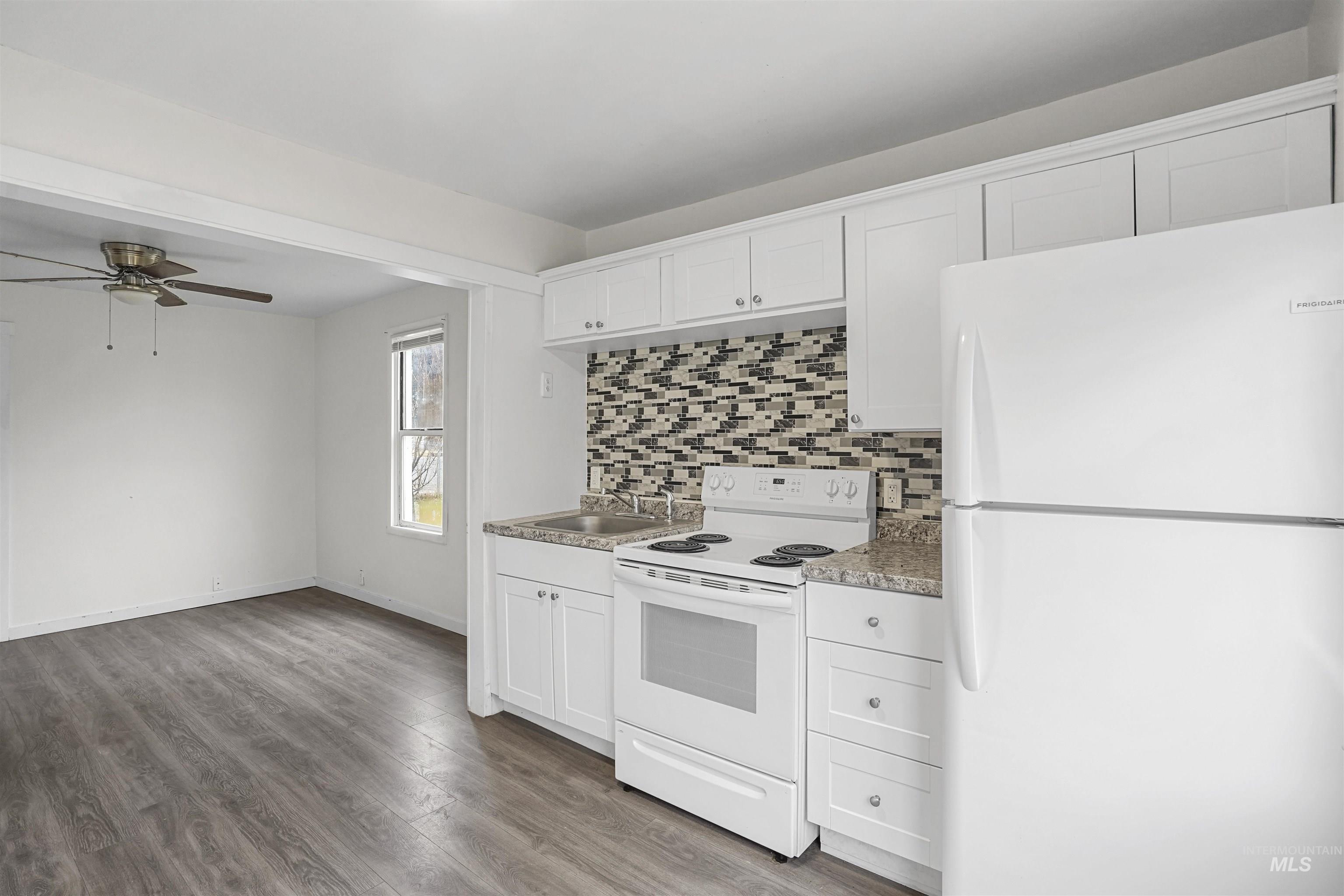 Kitchen with white appliances, white cabinets, backsplash, light wood-style flooring, and light countertops