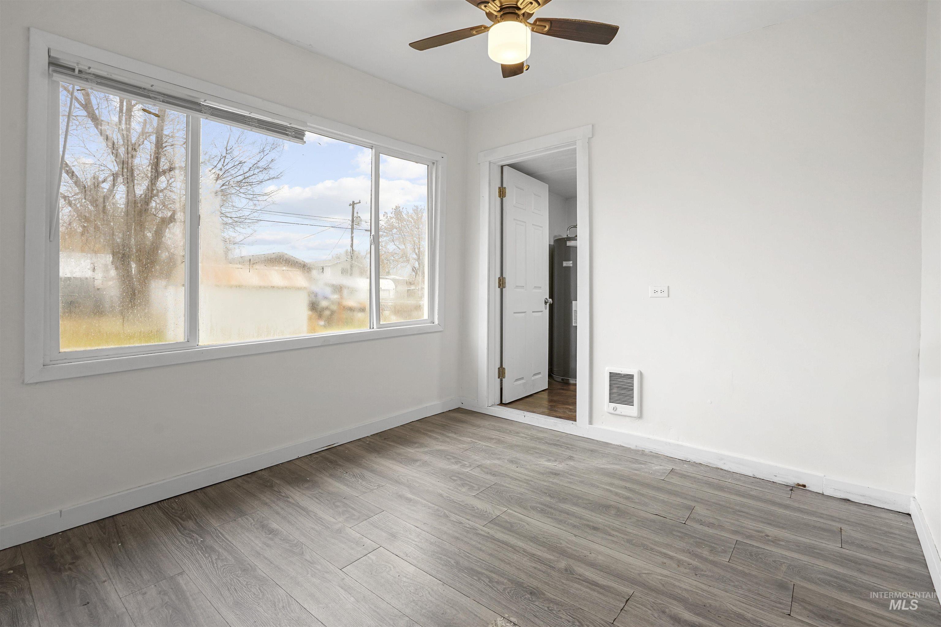 Empty room featuring wood finished floors, ceiling fan, heating unit, and water heater